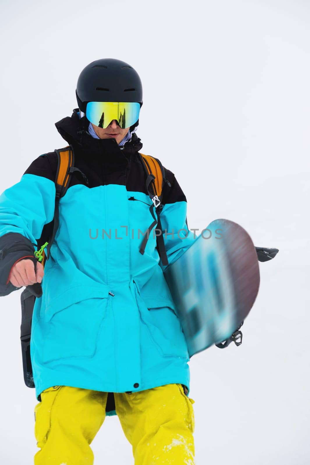 Close-up of a male snowboarder striding down the slope wearing a helmet and mask with his snowboard.
