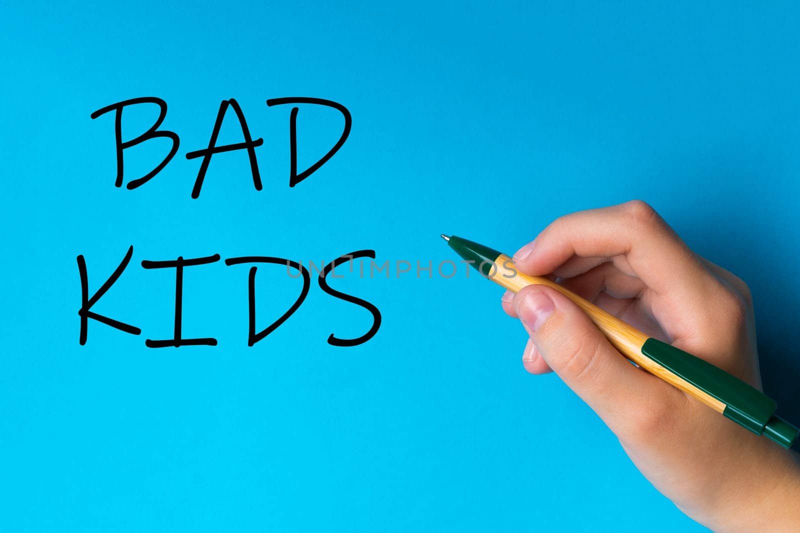 Children hand with pen write on an blue white background. Writing hand. Word Bad kids by Zelenin