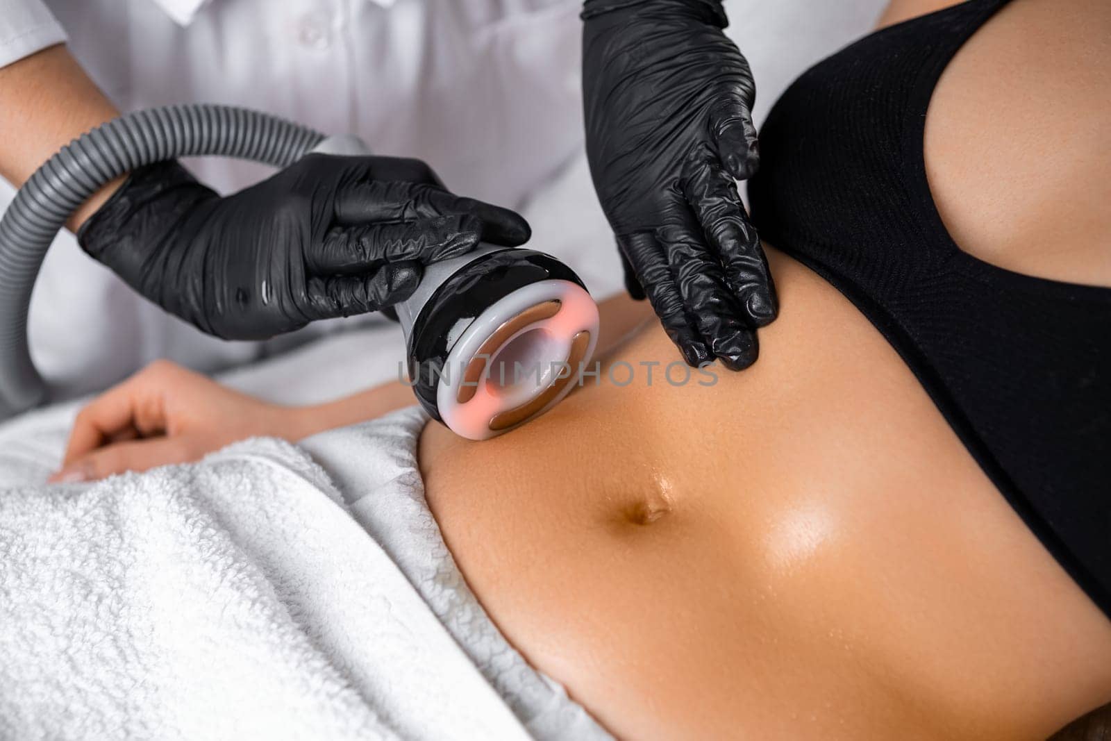 Close cosmetologist using ultrasound device while performing lifting procedure on woman belly.