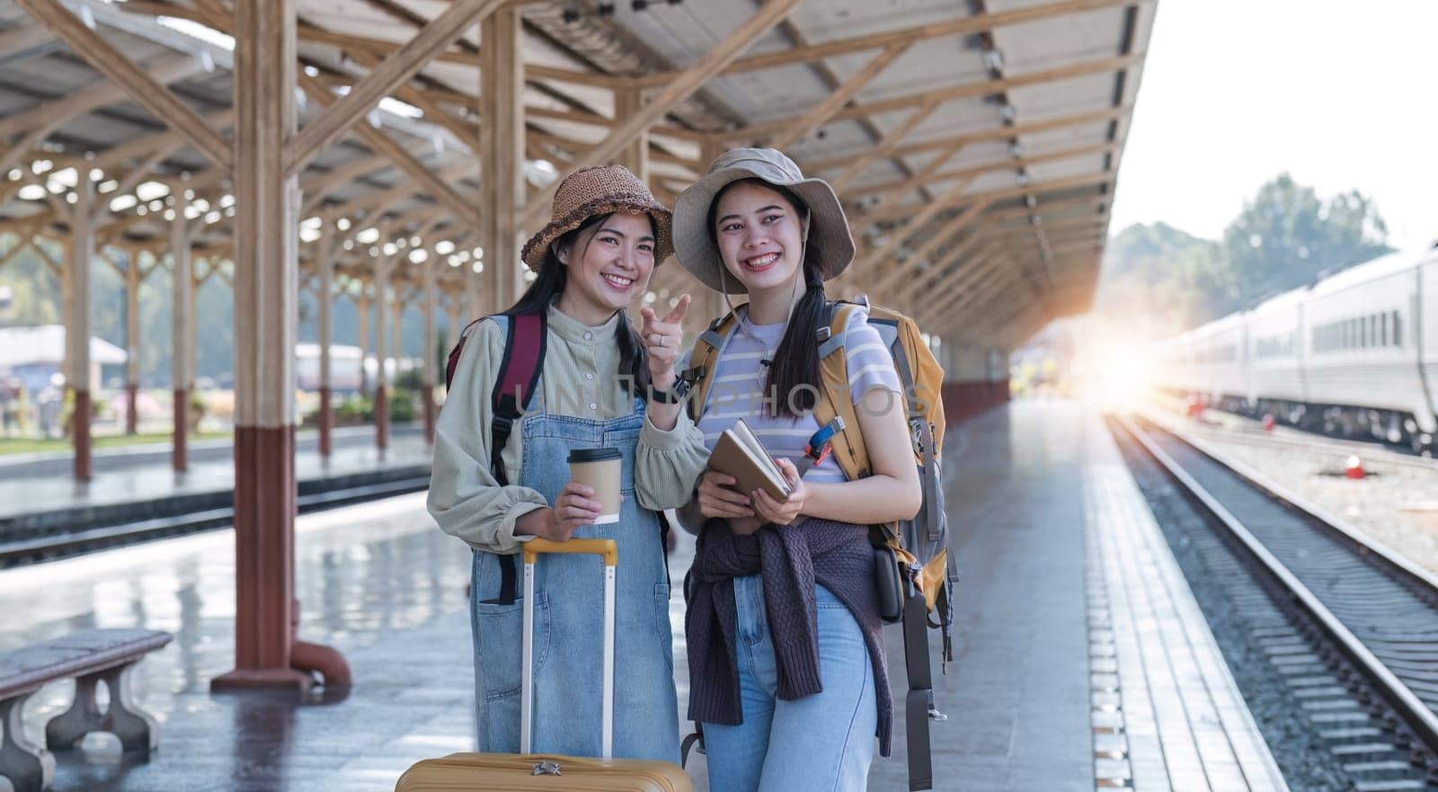 Two Asian female tourist friends are at the train station. Waiting for the train to travel to the provinces together on the weekend..