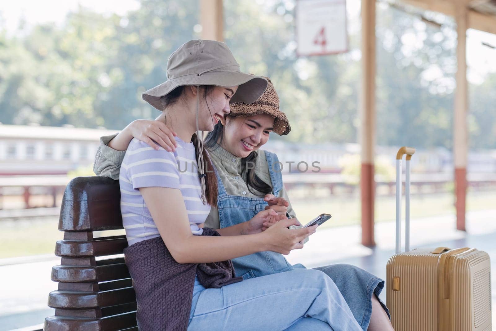 Two Asian female tourist friends are at the train station. Waiting for the train to travel to the provinces together on the weekend. by wichayada