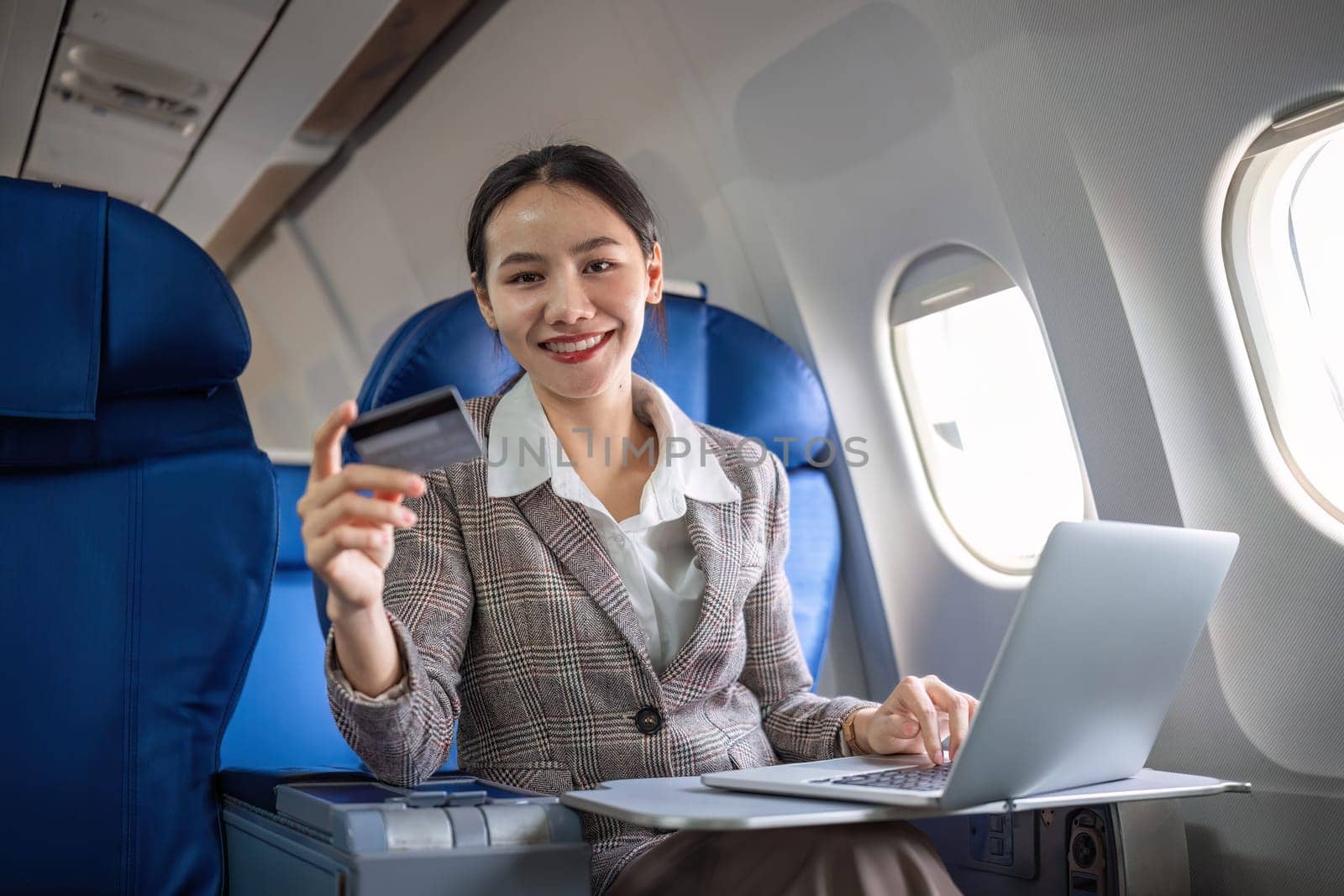 Young Asian woman holding credit card shopping online using website on laptop Sitting near window in first class on airplane during flight, travel and business concept..