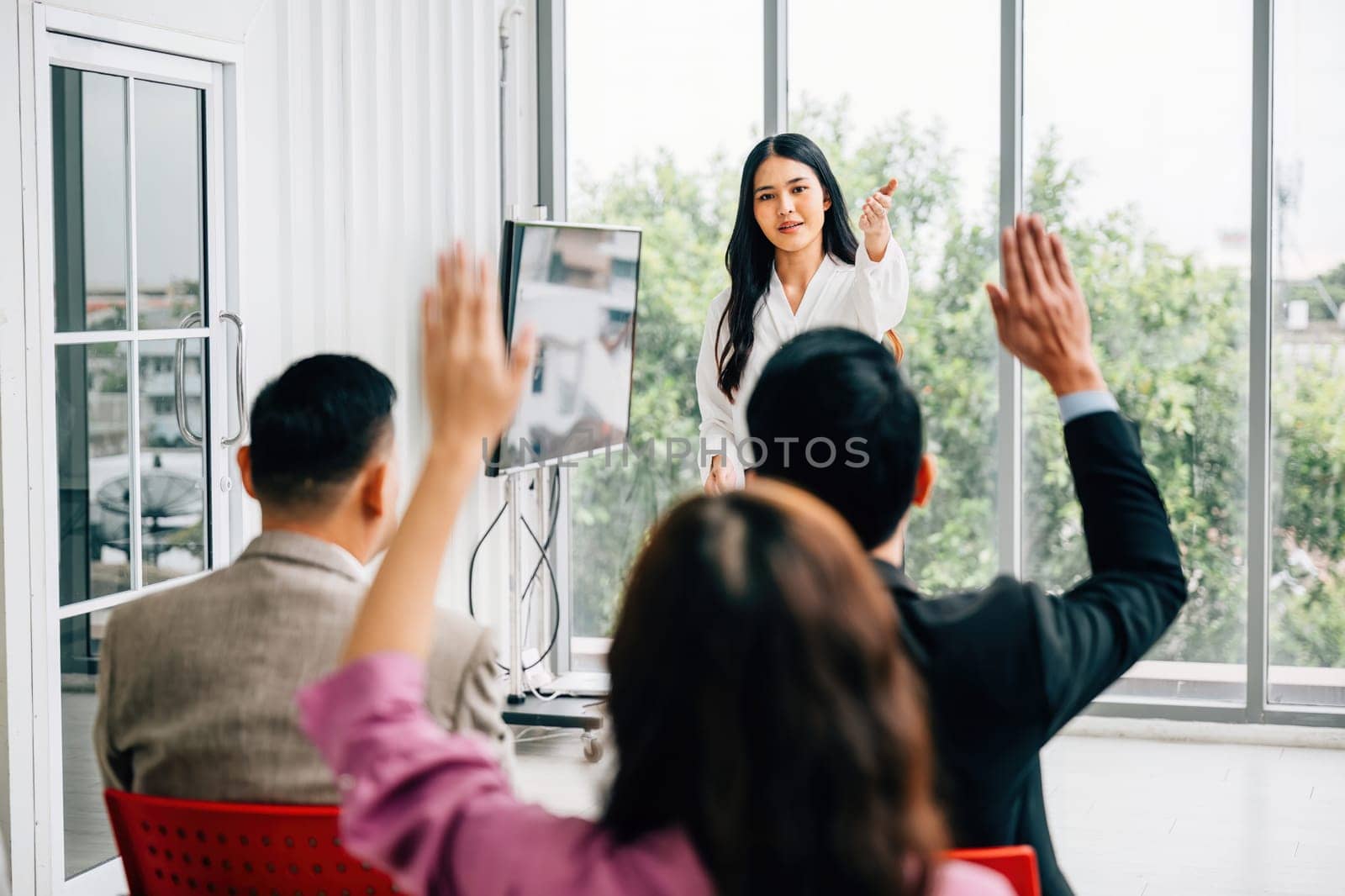 A seminar classroom hosts a large group actively engaging in the discussion, raising their hands. The answers are ready within this dynamic conference audience. by Sorapop