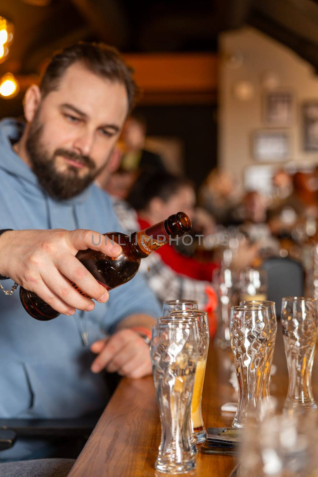 A young handsome man with a beard pouring beer from bottle by BY-_-BY