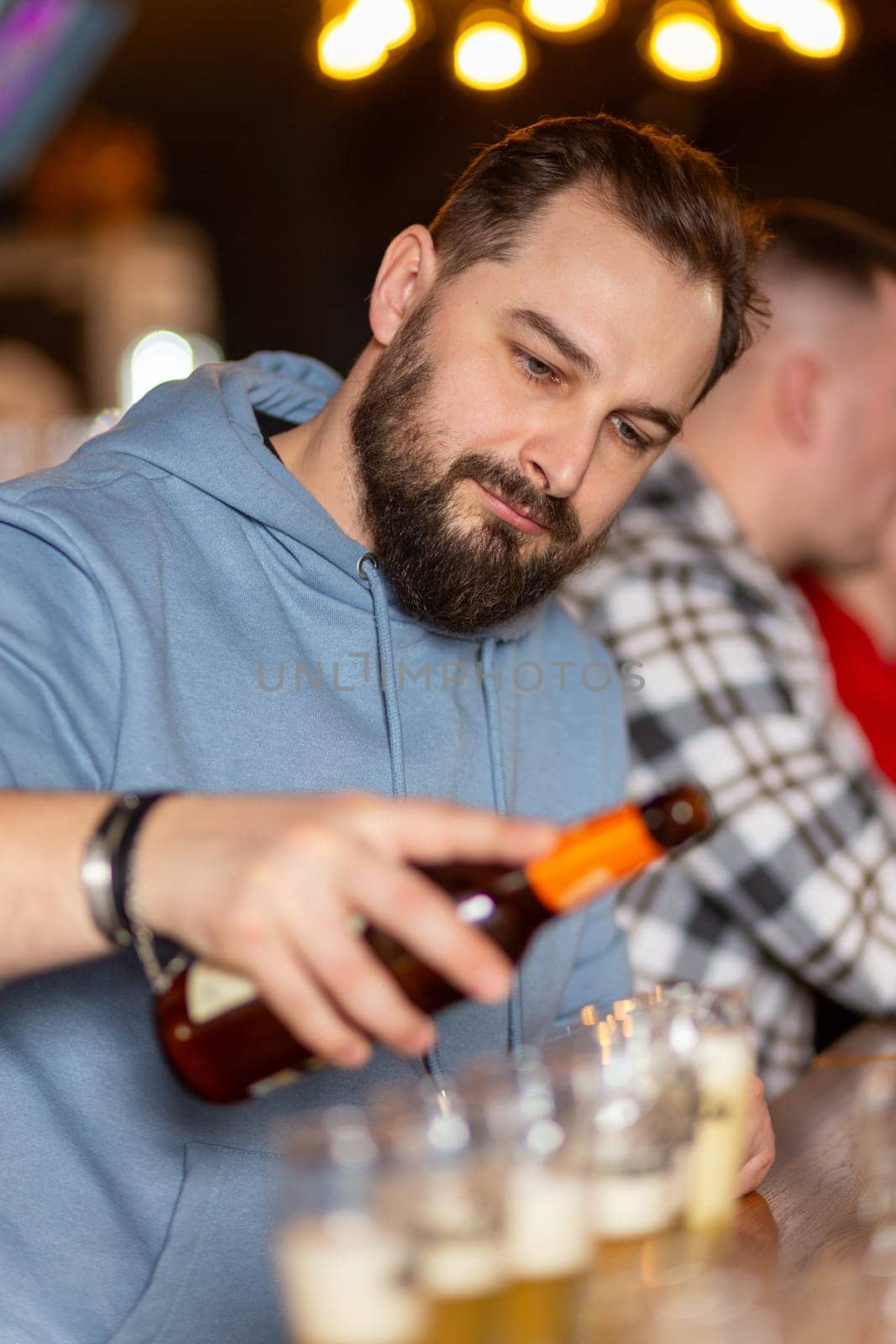 A young handsome man with a beard pouring beer from bottle by BY-_-BY