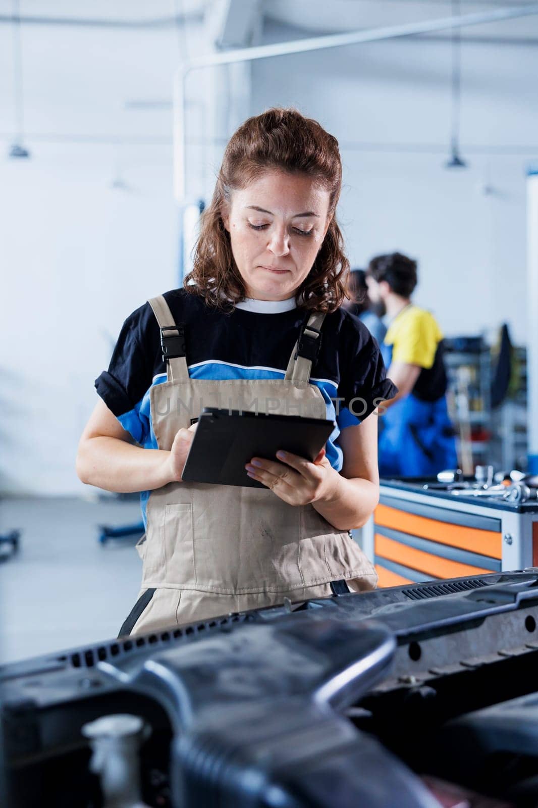 Technician in car service uses tablet to calculate invoice for client after repairing lights system. Skilled garage employee calculating final costs after servicing customer vehicle