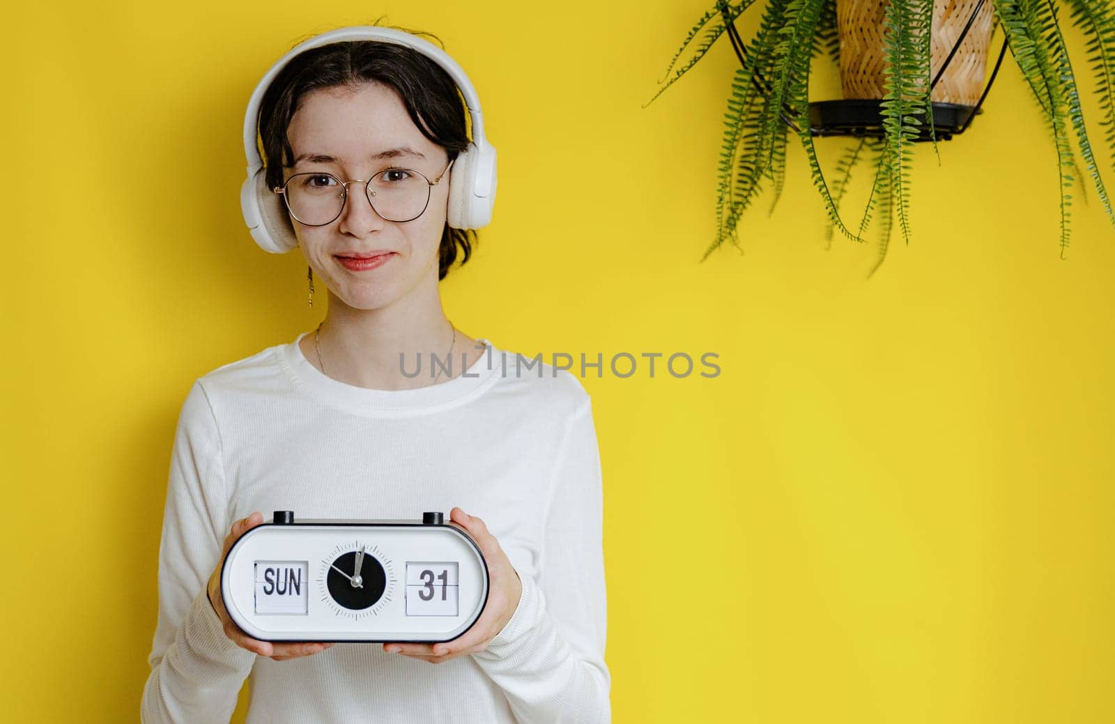 A teenage girl holds an alarm clock with the time, day and date: Sunday, lunch, 31. by Nataliya