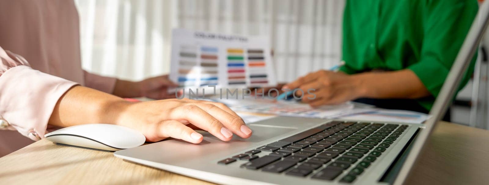 Creative graphic design presents selective color while manager using laptop comparing suitable color at table with color palettes, graphic material scatter around at modern office. Variegated.
