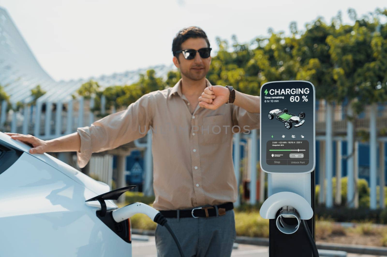 Young man put EV charger to recharge electric car's battery from charging station in city commercial parking lot. Rechargeable EV car for sustainable environmental friendly urban travel. Expedient