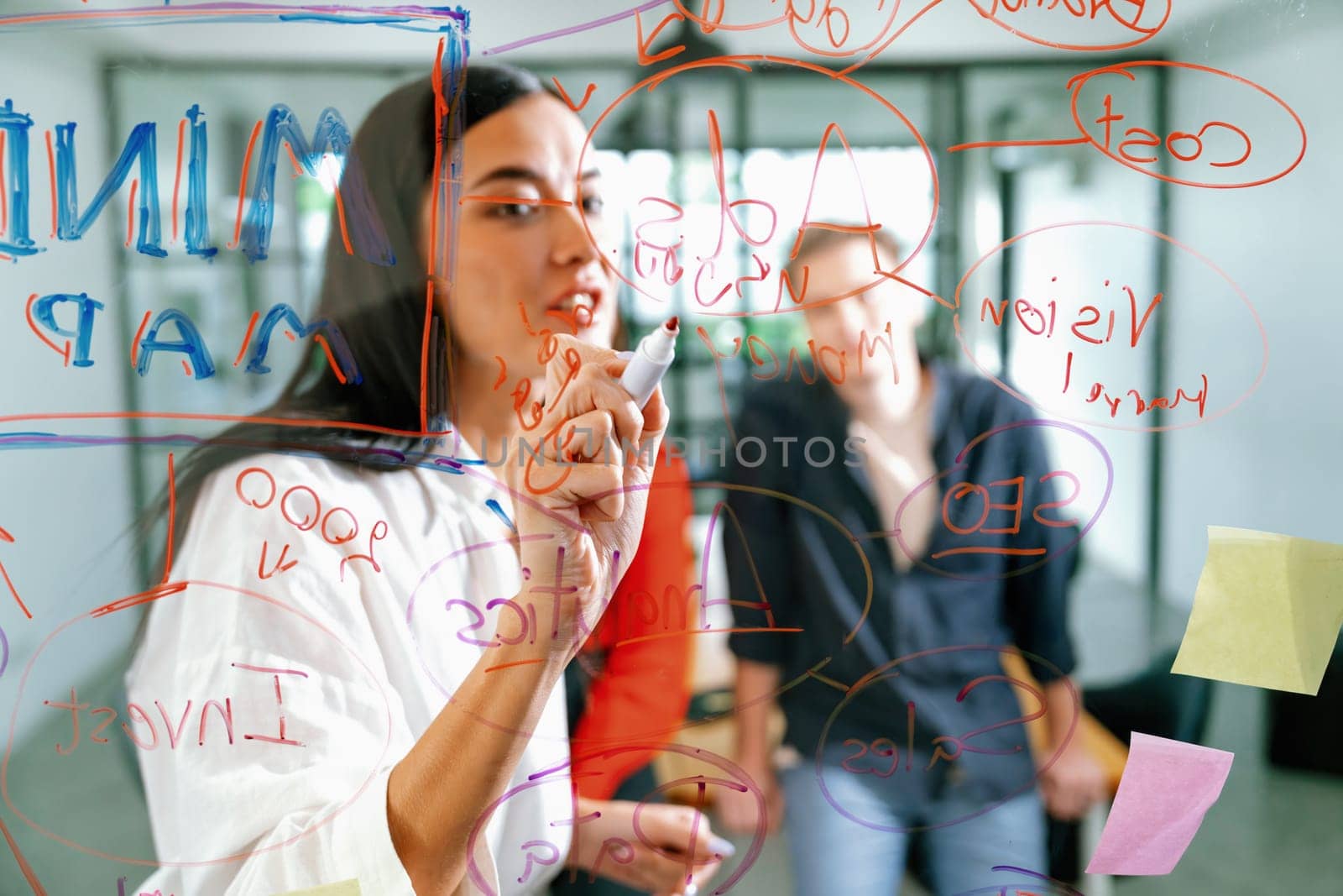 Professional business team brainstorming and working together about marketing project. Female caucasian leader writing idea on stick note while coworker present her idea confidently. Immaculate.
