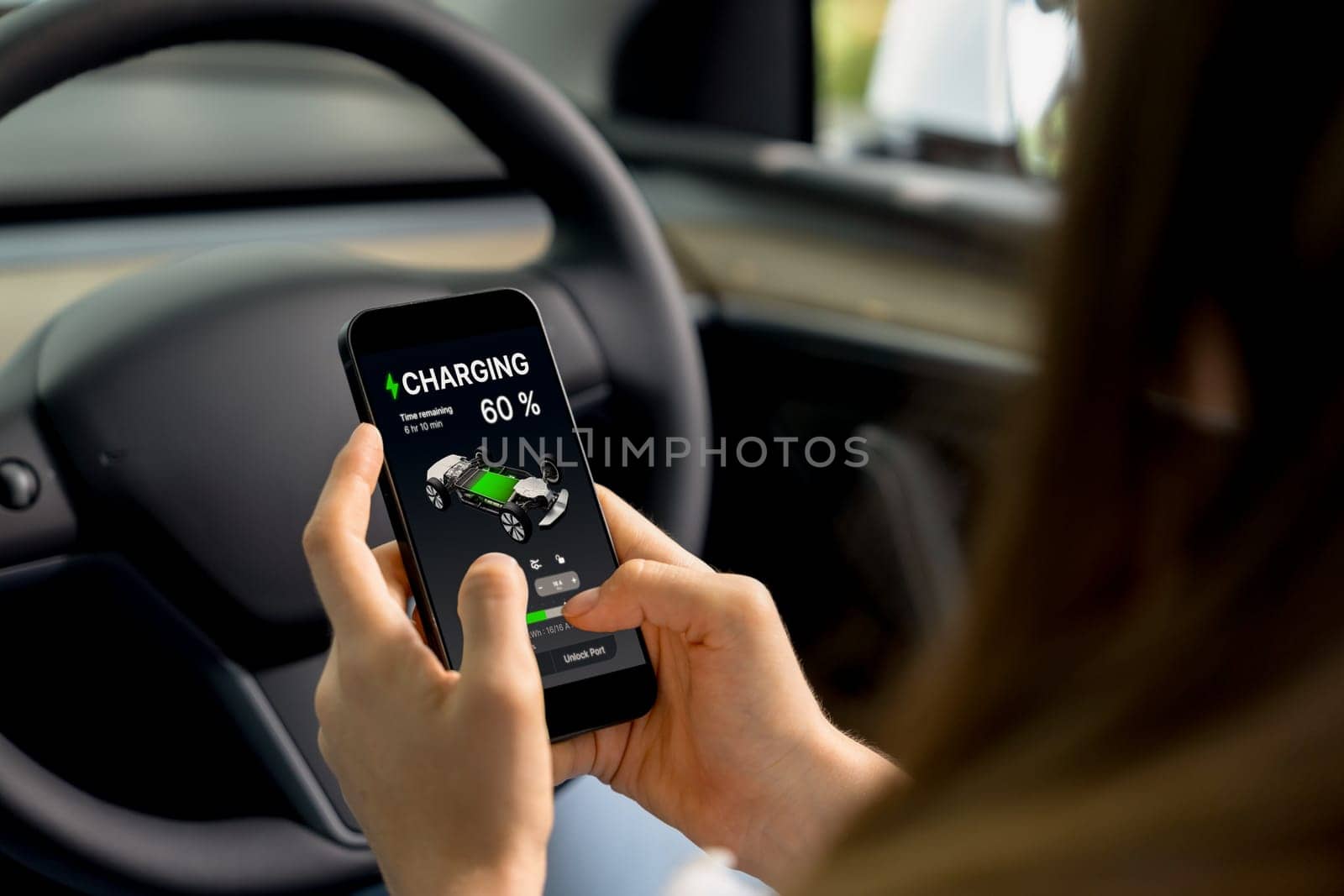 Young woman inside the vehicle, checking EV vehicle's application on battery recharging electricity status display on smartphone screen in modern EV car on her road trip journey. Exalt