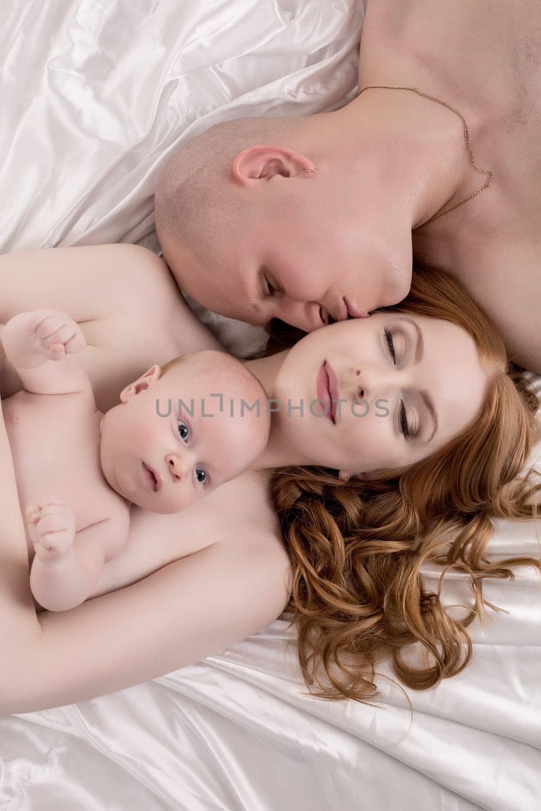 Top view of happy parents and baby. Man kisses his wife