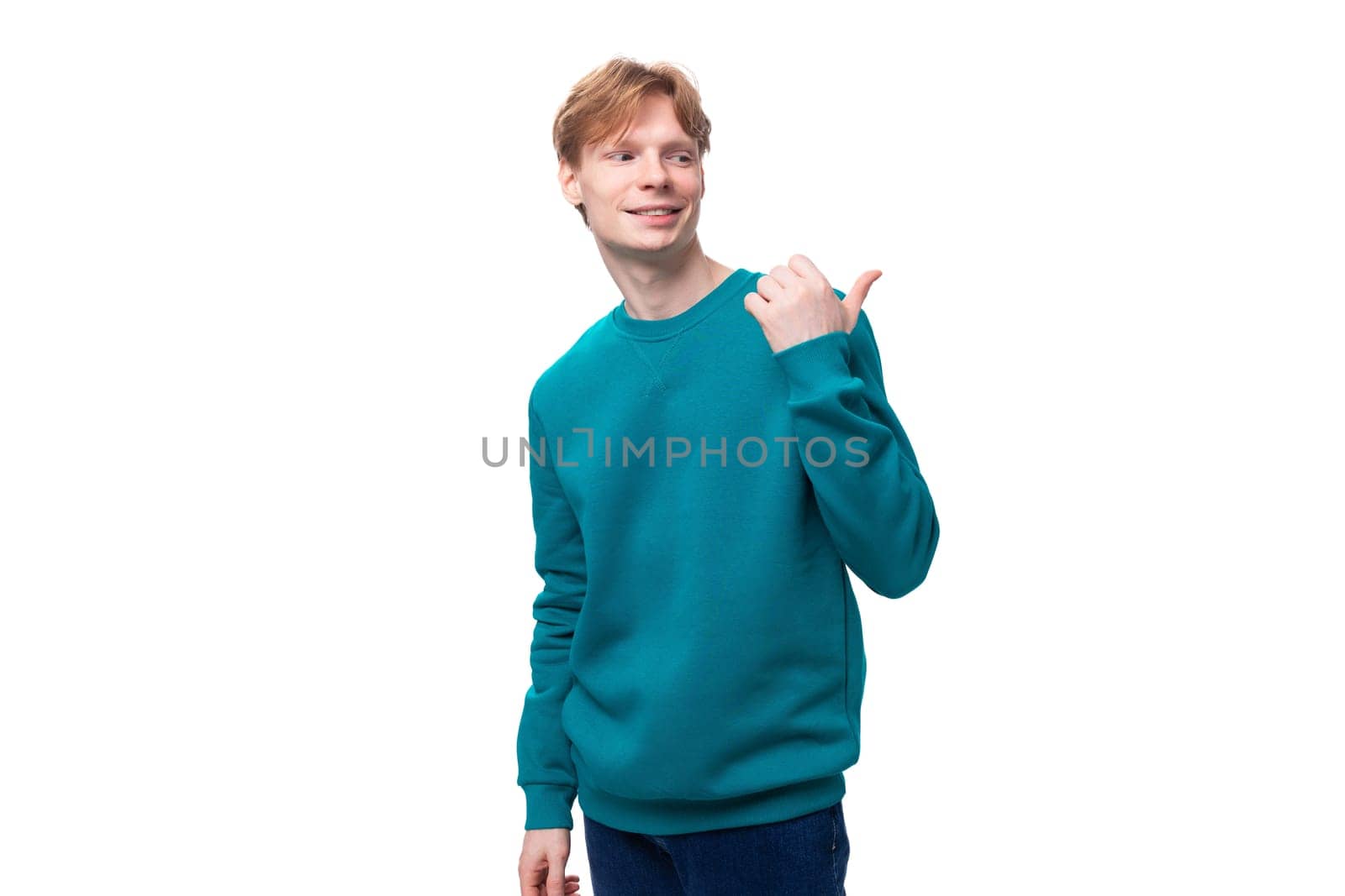 young caucasian student guy with red hair in a blue sweater points with his hand at the space for advertising by TRMK