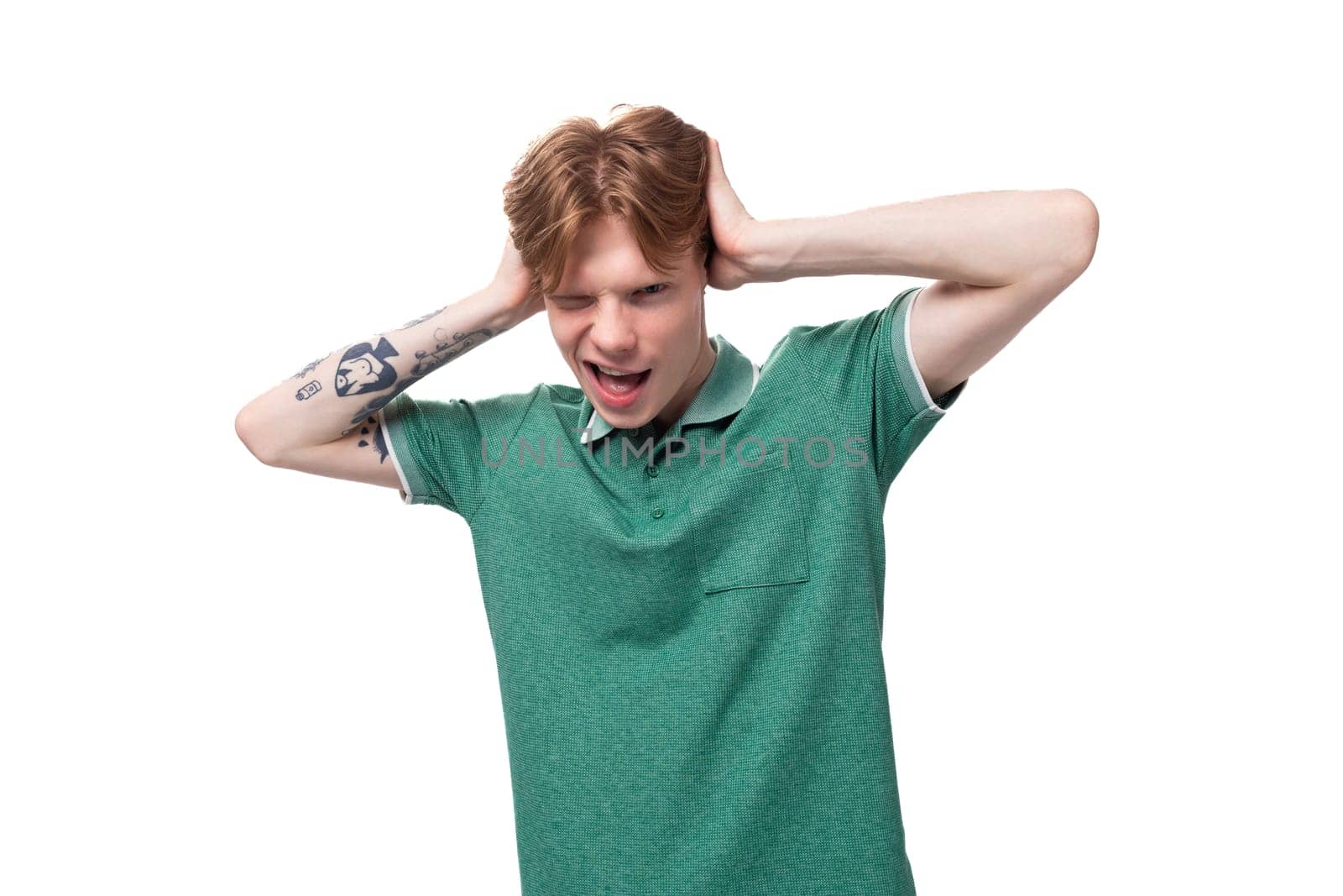 young charming adorable ginger man with a tattoo on his arm dressed in a green short sleeve t-shirt covers his ears with his hands by TRMK