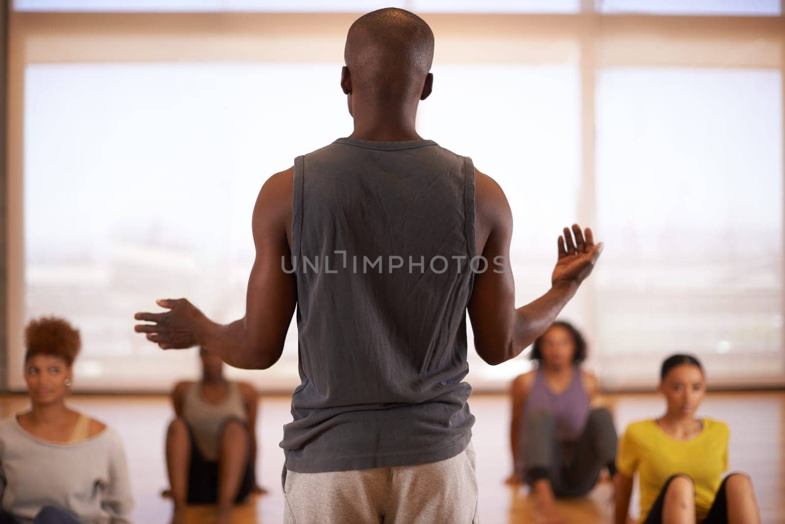 People, dancer and instructor with class of students in fitness, workout or pilates at the studio. Rear view of personal trainer talking to group in body warm up or stretching for health and wellness.