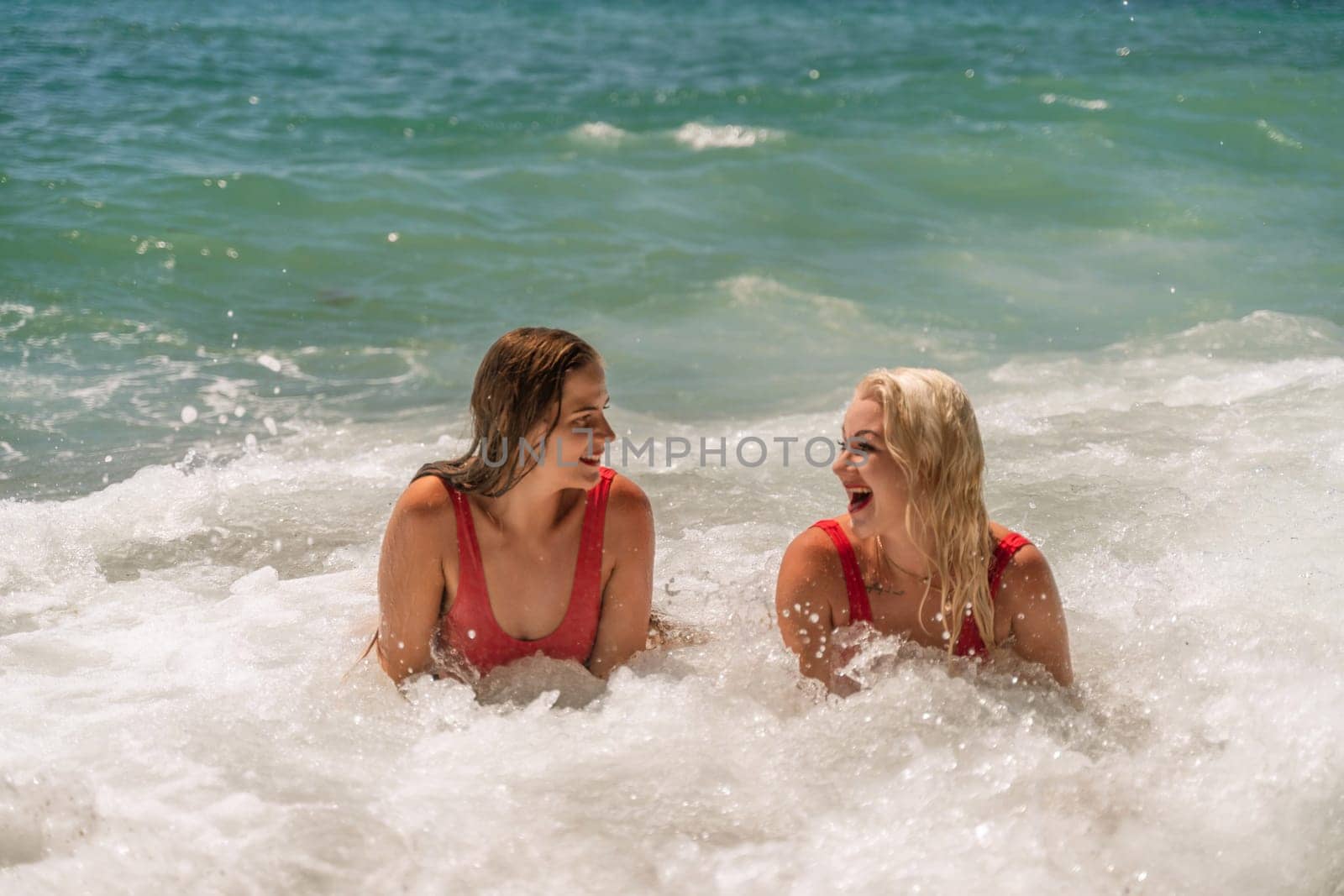 Women ocean play. Seaside, beach daytime, enjoying beach fun. Two women in red swimsuits enjoying themselves in the ocean waves. by Matiunina