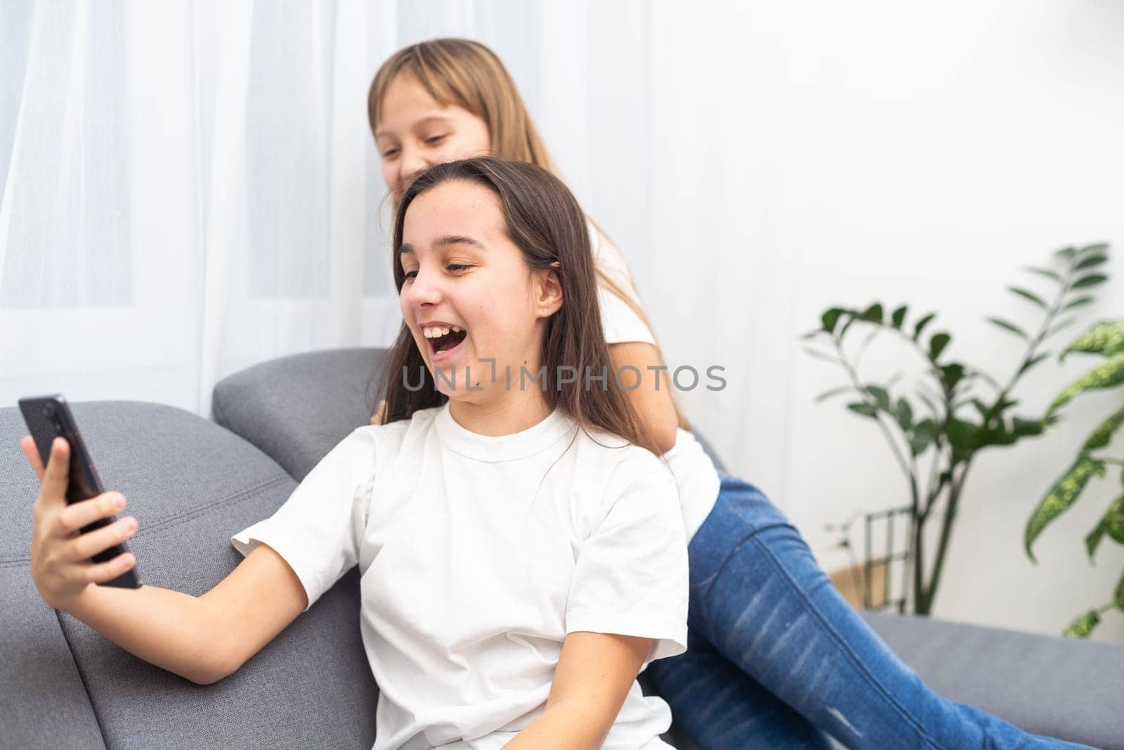Child with smartphone at home. Two kids using smart phone, surfing internet or using social media. Two kids using online mobile phone, call, watching content, playing video games, sitting on couch. High quality photo