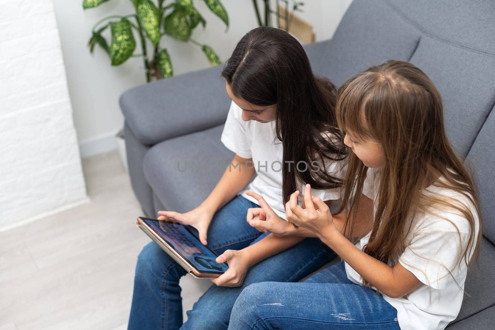 Shocked sisters using digital tablet on sofa at home. High quality photo