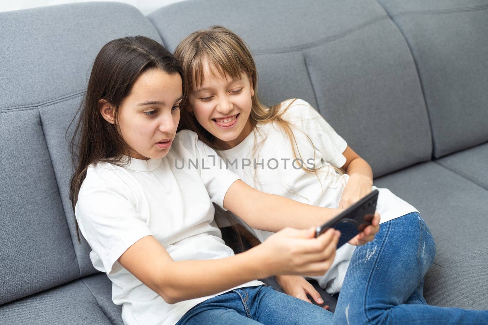 Child with smartphone at home. Two kids using smart phone, surfing internet or using social media. Two kids using online mobile phone, call, watching content, playing video games, sitting on couch by Andelov13