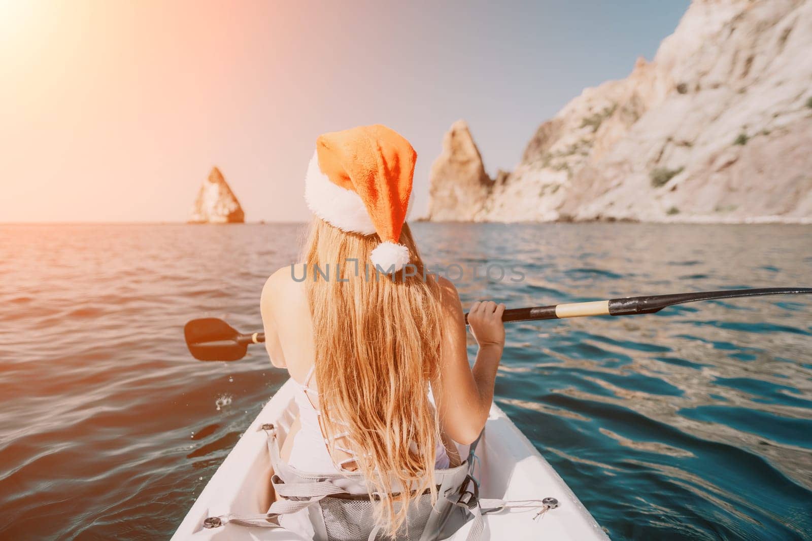 Woman in kayak back view. Happy young woman with long hair floating in transparent kayak on the crystal clear sea. Summer holiday vacation and cheerful female people relaxing having fun on the boat