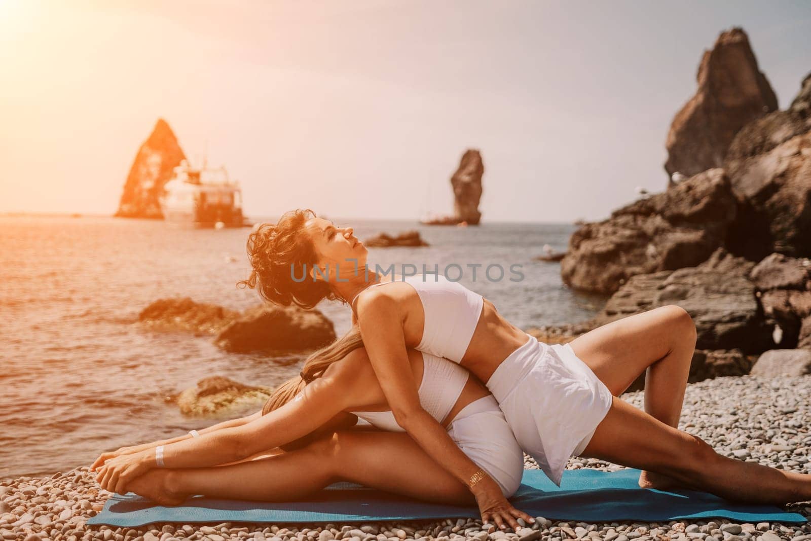 Woman sea yoga. Two happy women practicing yoga on the beach with ocean and rock mountains. Motivation and inspirational fit and exercising. Healthy lifestyle outdoors in nature, fitness concept. by panophotograph