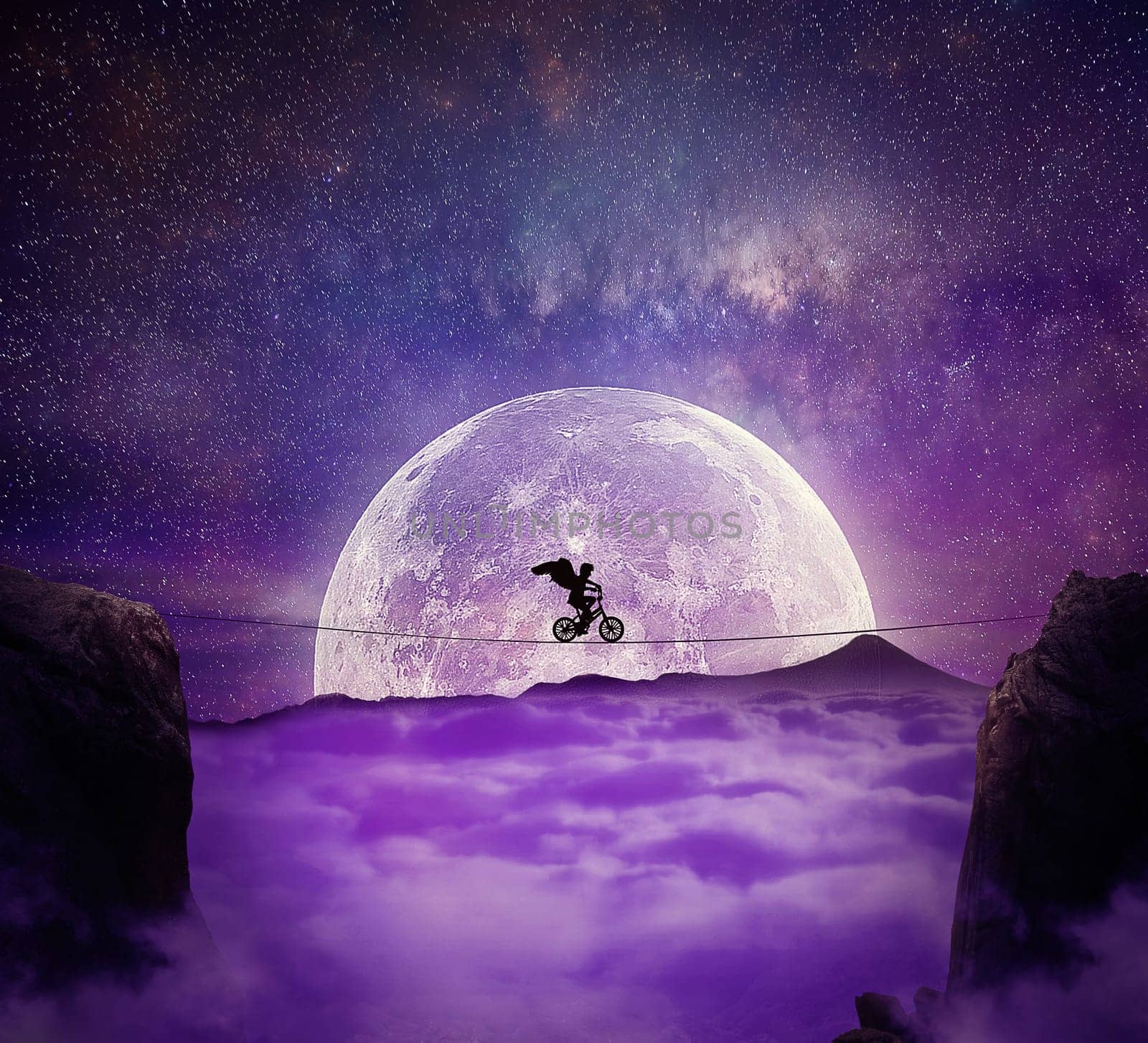 Boy with angel wings balance on a wire over a chasm riding a bicycle. Self overcoming and risk taking concept. Full moon night background over the clouds