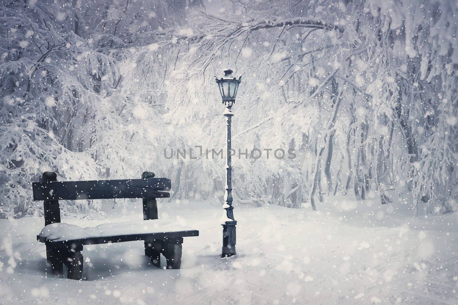 Winter time scene with a wooden bench and street lamp covered with snow under a snowfall in the park. Wonderful holiday season background, Merry Christmas magic atmosphere. Tranquil and peaceful view