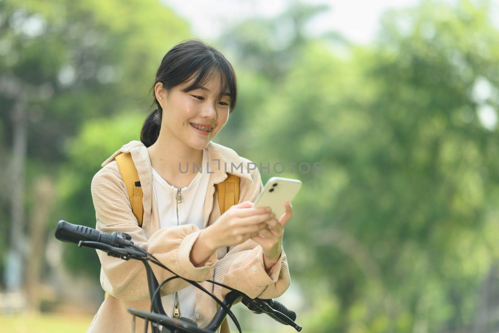 Attractive young woman standing near a bicycle at a city park and using a mobile phone by prathanchorruangsak