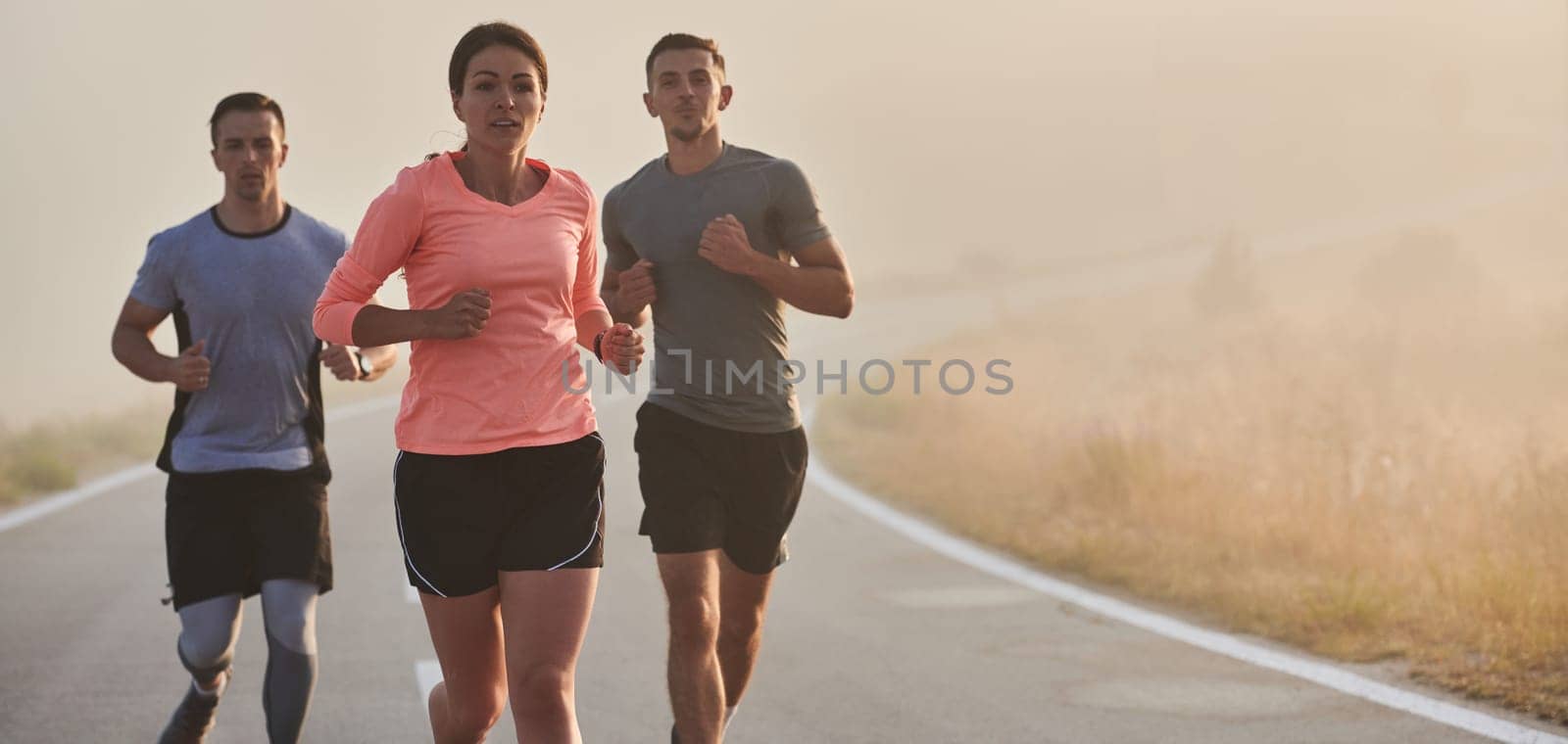 A group of friends, athletes, and joggers embrace the early morning hours as they run through the misty dawn, energized by the rising sun and surrounded by the tranquil beauty of nature.