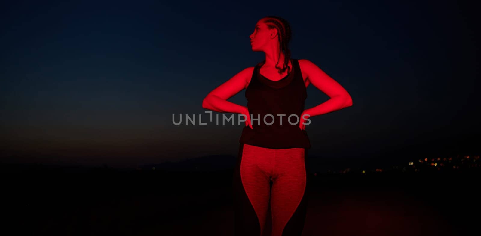 After a grueling nighttime run, an athlete strikes a confident pose, bathed in the red glow of the surroundings, showcasing both exhaustion and determination.