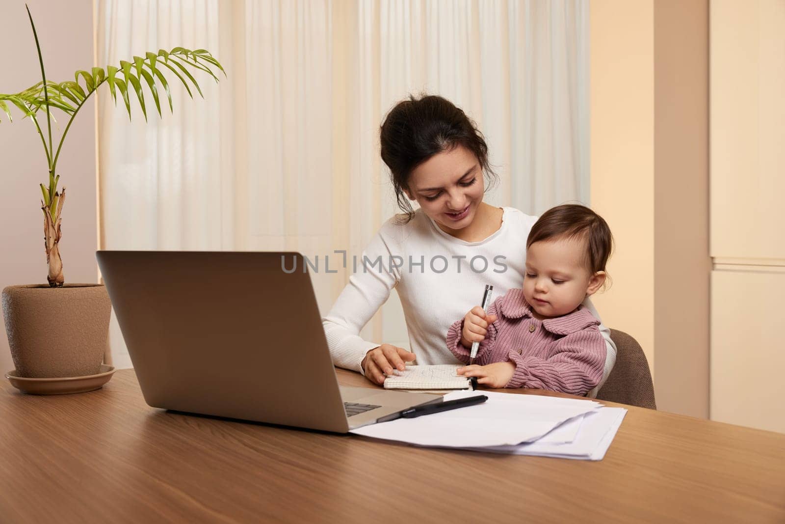 Cheerful pretty businesswoman working on laptop at home with her little child girl