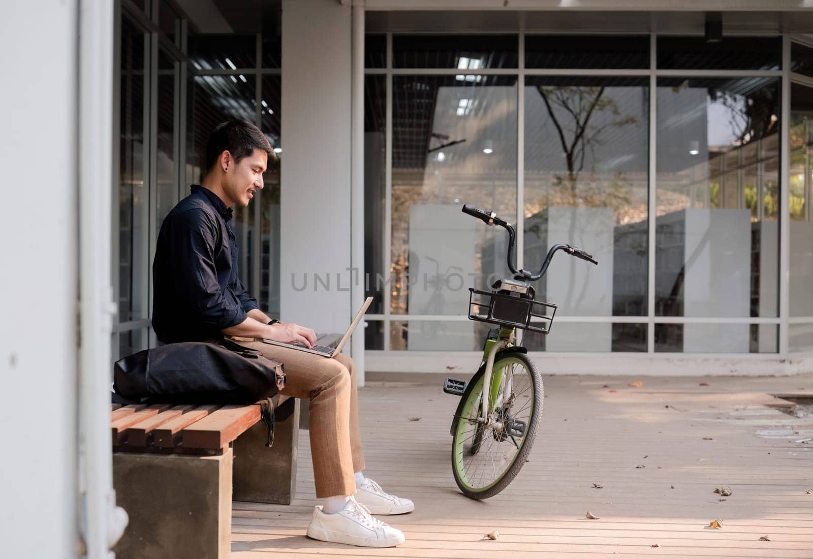 A young Asian businessman rides a bicycle to work. Use a reusable water bottle. Working outside of the office using a laptop The concept of saving energy and reducing pollution to the environment..