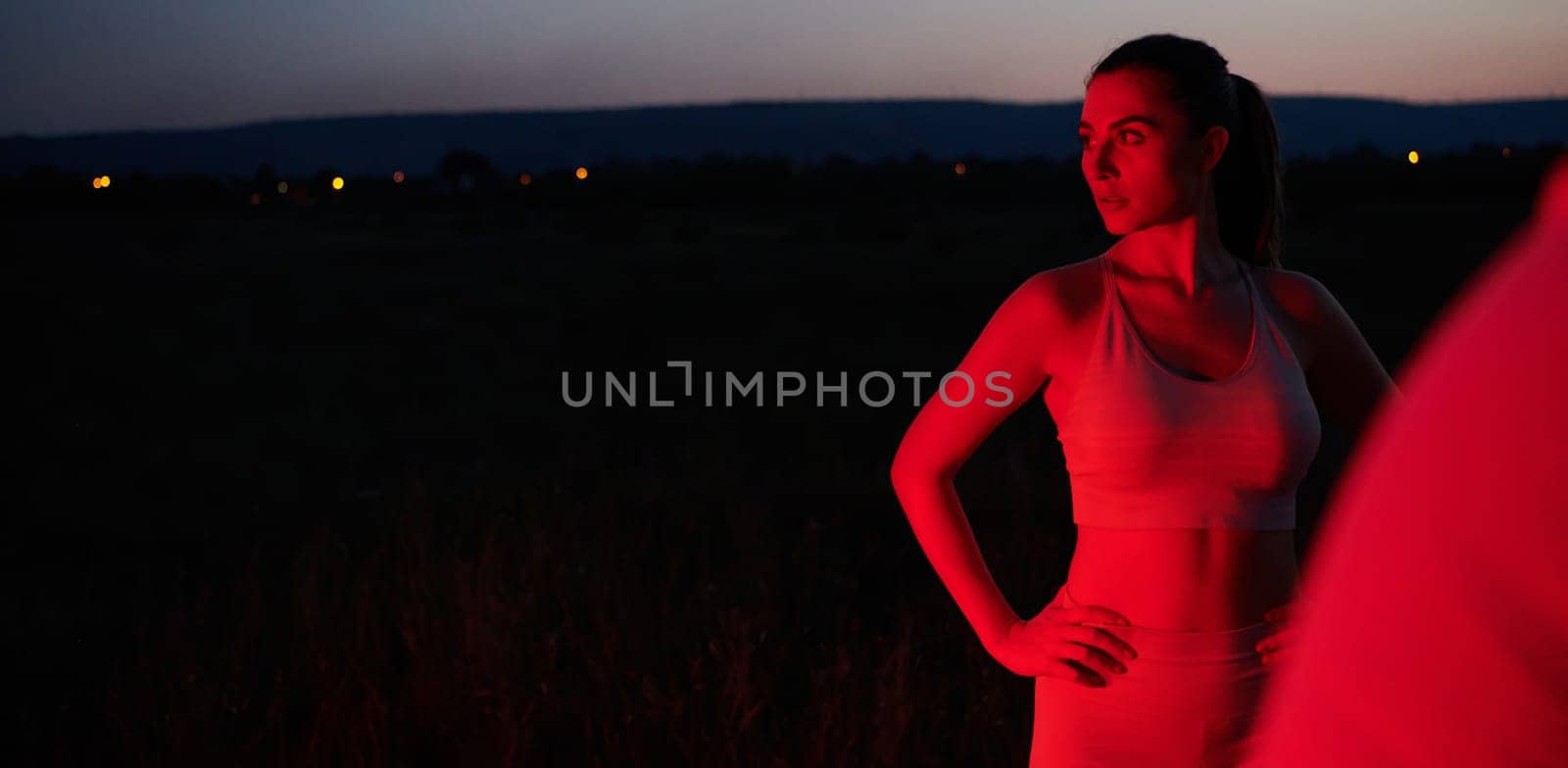 After a grueling nighttime run, an athlete strikes a confident pose, bathed in the red glow of the surroundings, showcasing both exhaustion and determination.