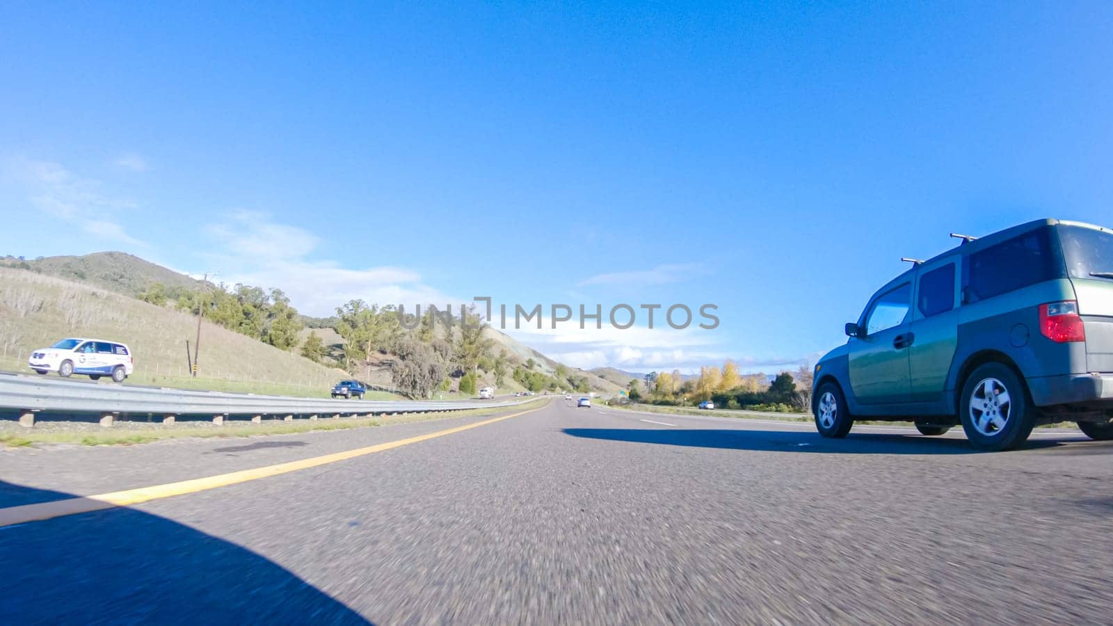 Santa Maria, California, USA-December 6, 2022-On a crisp winter day, a car cruises along the iconic Highway 1 near San Luis Obispo, California. The surrounding landscape is brownish and subdued, with rolling hills and patches of coastal vegetation flanking the winding road.