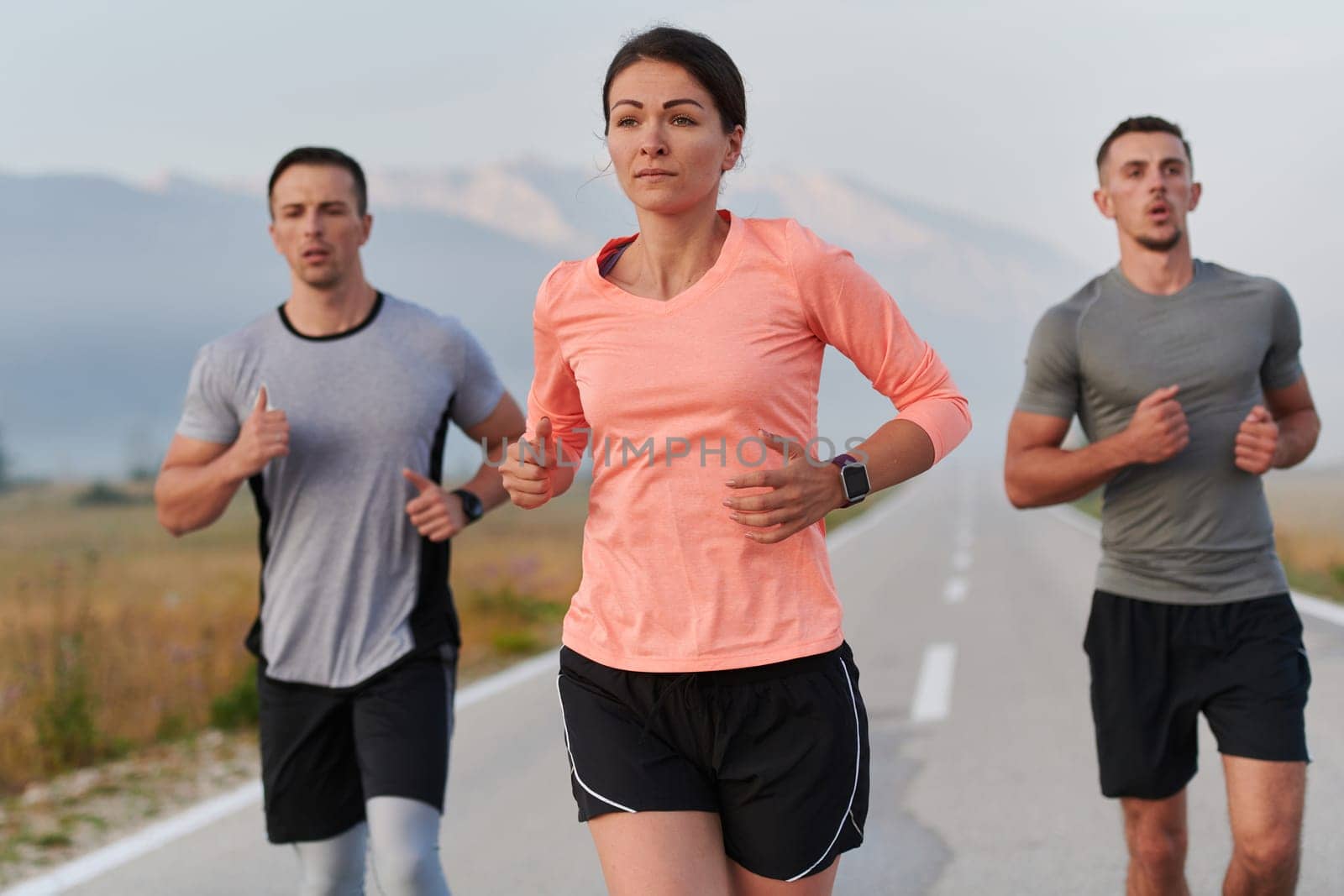 A group of friends, athletes, and joggers embrace the early morning hours as they run through the misty dawn, energized by the rising sun and surrounded by the tranquil beauty of nature.