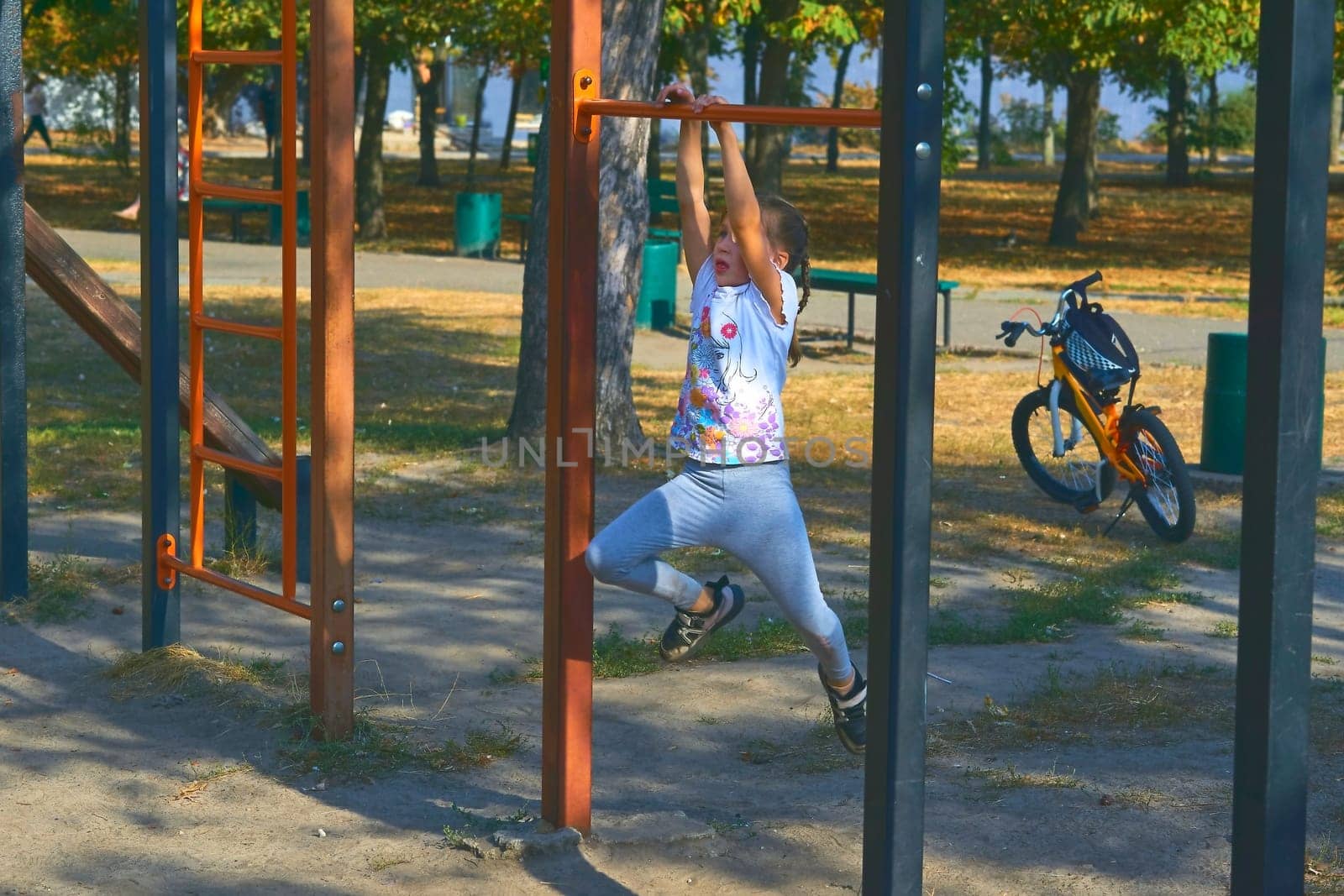 A cheerful child girl is working out on the horizontal bar, sports apparatus by jovani68