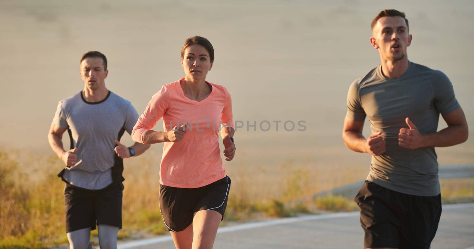 A group of friends, athletes, and joggers embrace the early morning hours as they run through the misty dawn, energized by the rising sun and surrounded by the tranquil beauty of nature.