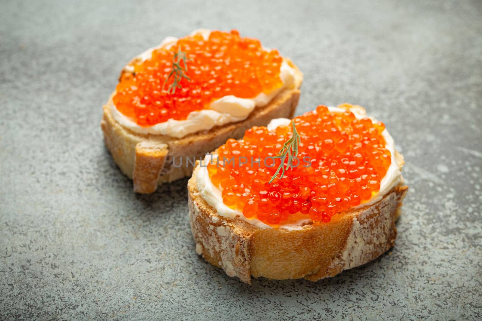 Two caviar toasts baguette canape with butter and red salmon caviar top view on grey concrete background, festive luxury delicacy and appetizer by its_al_dente