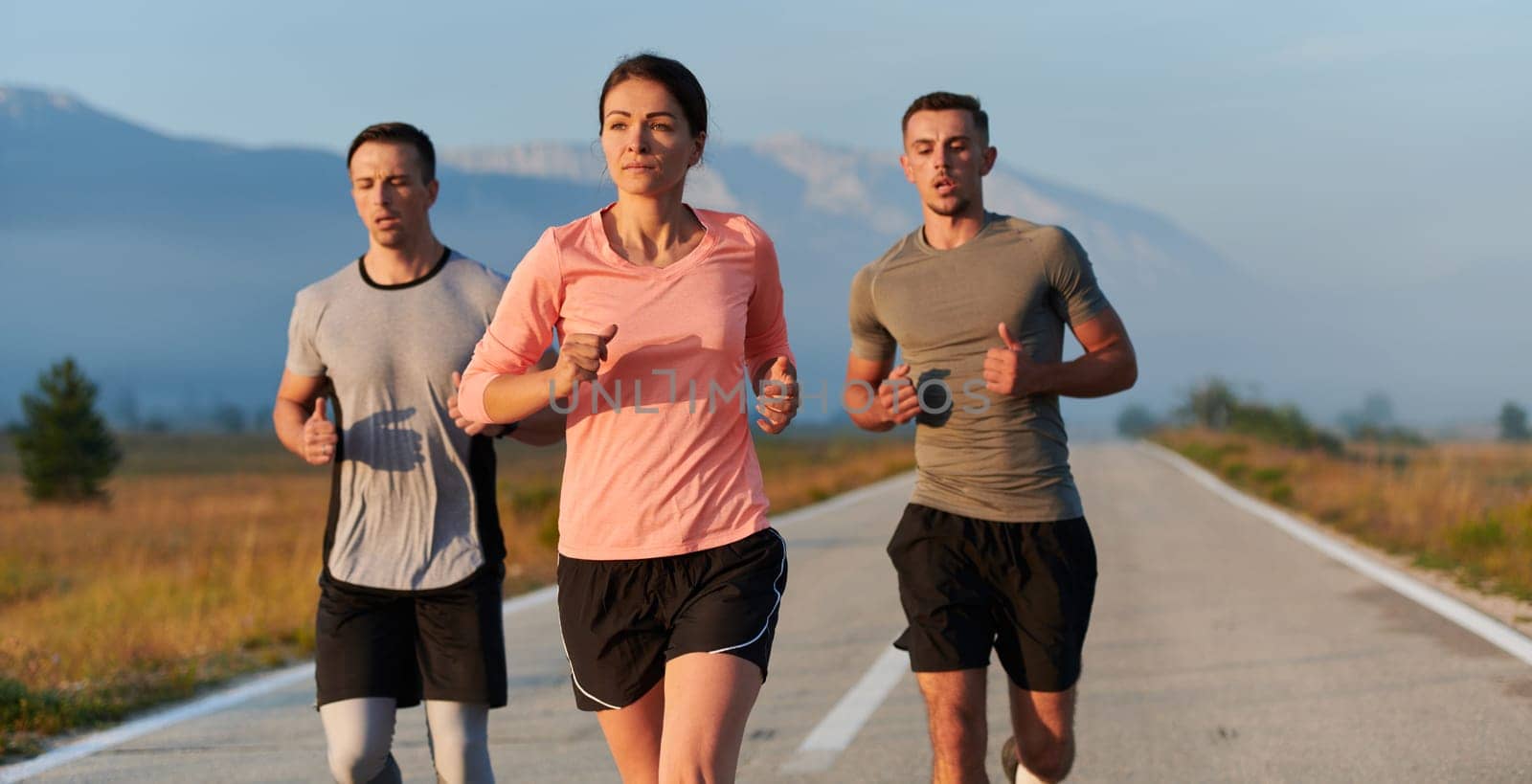 A group of friends, athletes, and joggers embrace the early morning hours as they run through the misty dawn, energized by the rising sun and surrounded by the tranquil beauty of nature.