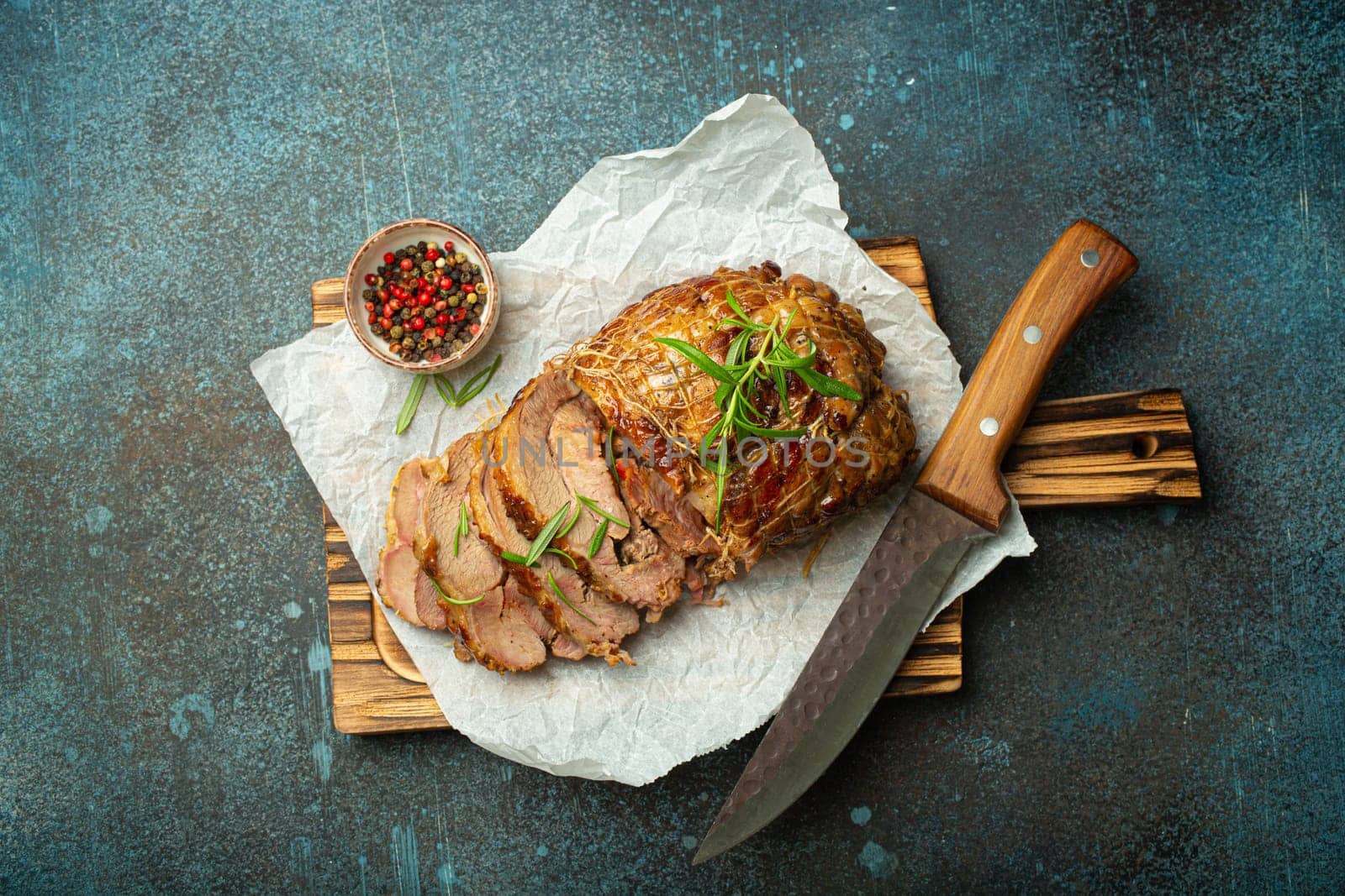 Rolled turkey roasted with spices and herbs on baking paper with knife and rustic concrete background top view. Baked cut for slices turkey fillet roll for dinner.