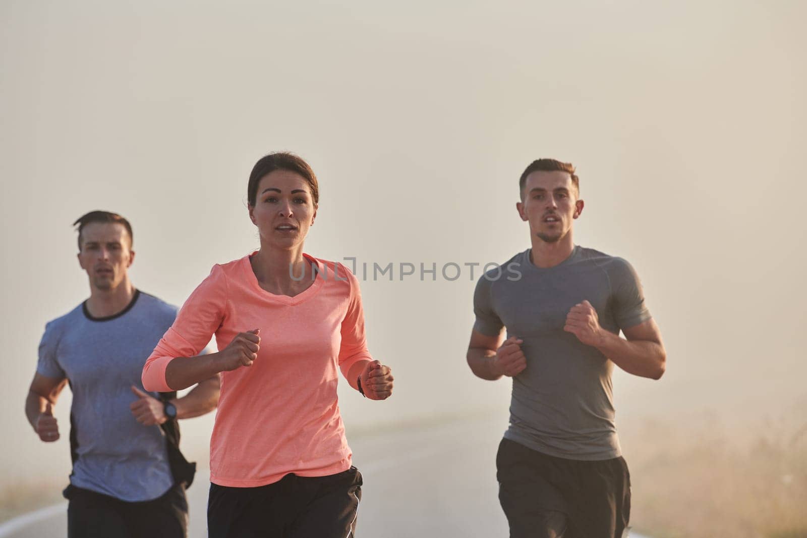 A group of friends, athletes, and joggers embrace the early morning hours as they run through the misty dawn, energized by the rising sun and surrounded by the tranquil beauty of nature.