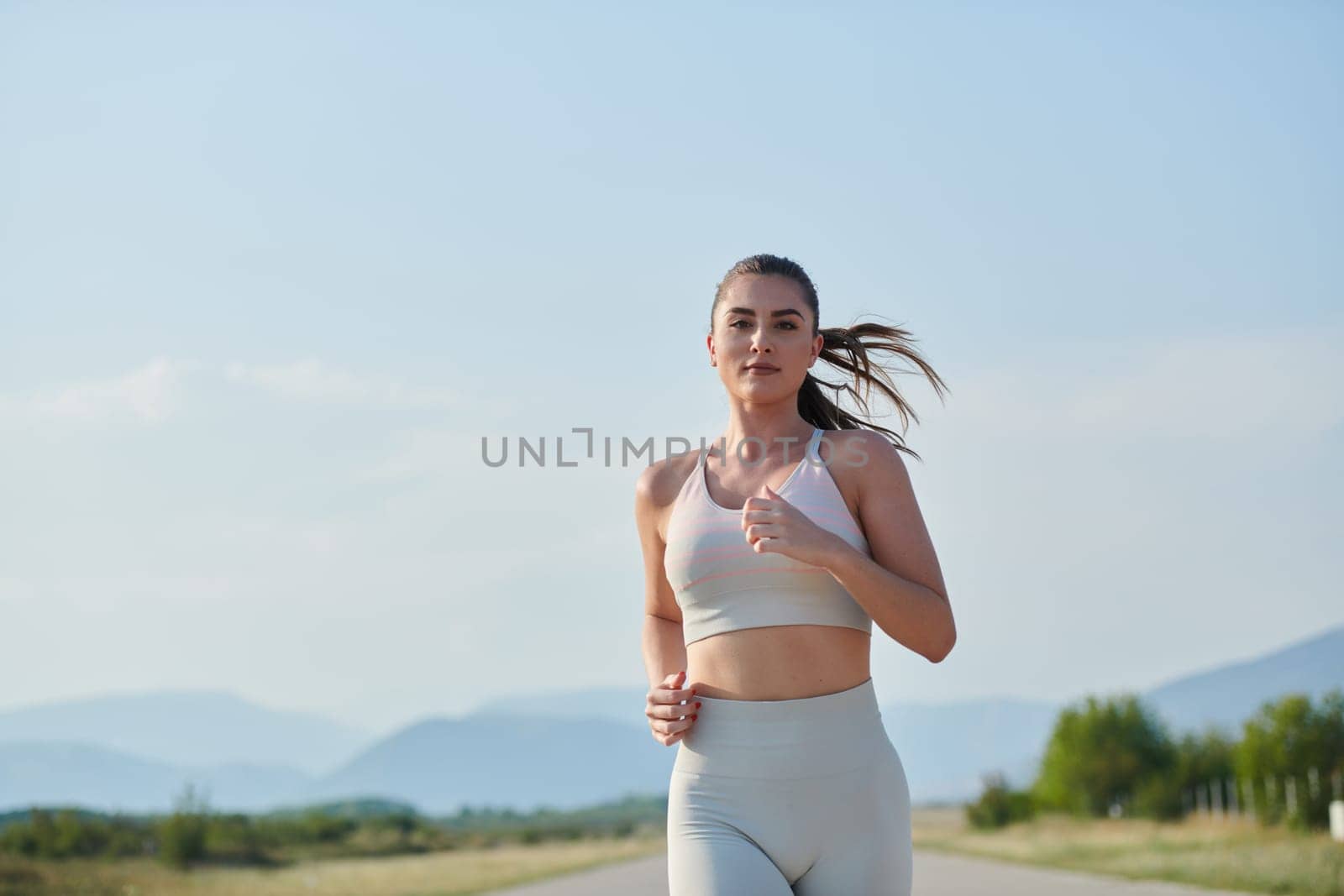 An athletic woman finds freedom and joy in a healthy lifestyle, running through a beautiful road trail at sunrise.