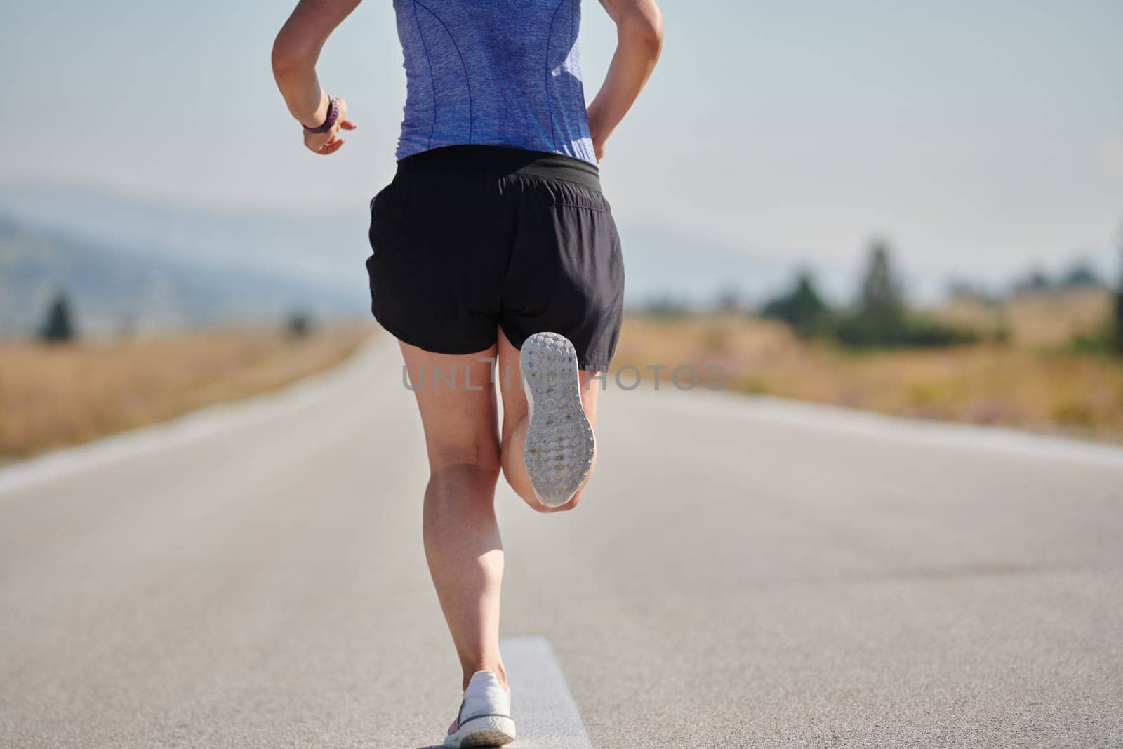 An athletic woman finds freedom and joy in a healthy lifestyle, running through a beautiful road trail at sunrise.