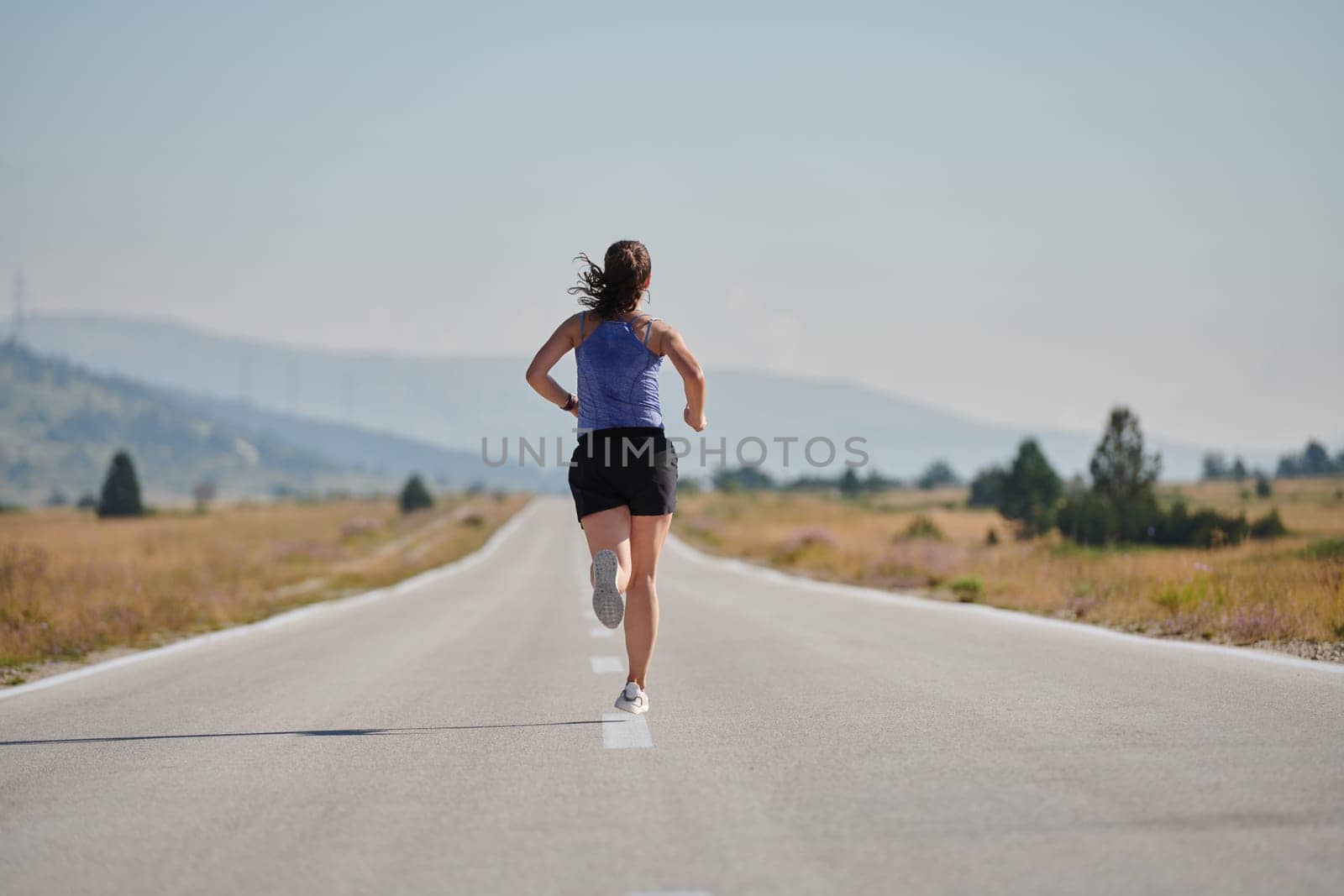 An athletic woman finds freedom and joy in a healthy lifestyle, running through a beautiful road trail at sunrise.