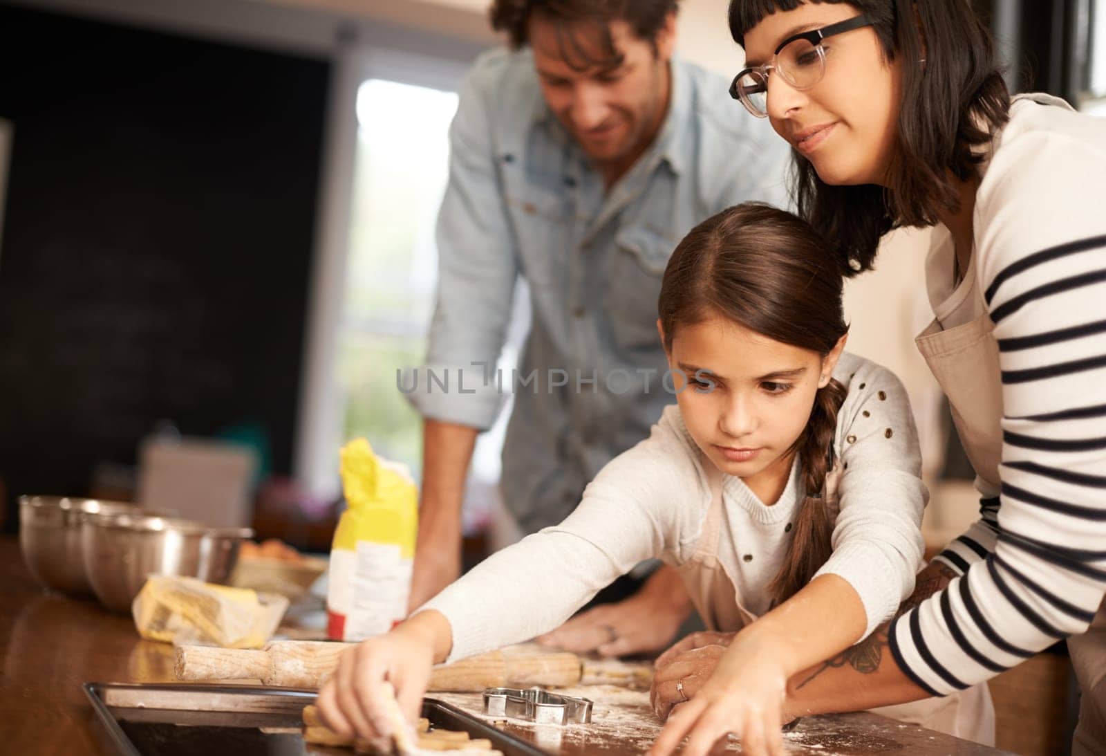 Mother, father and girl with baking cookies in kitchen with pan, happiness and teaching with support. Family, parents and child with helping, learning and bonding with cooking for dinner and snack by YuriArcurs