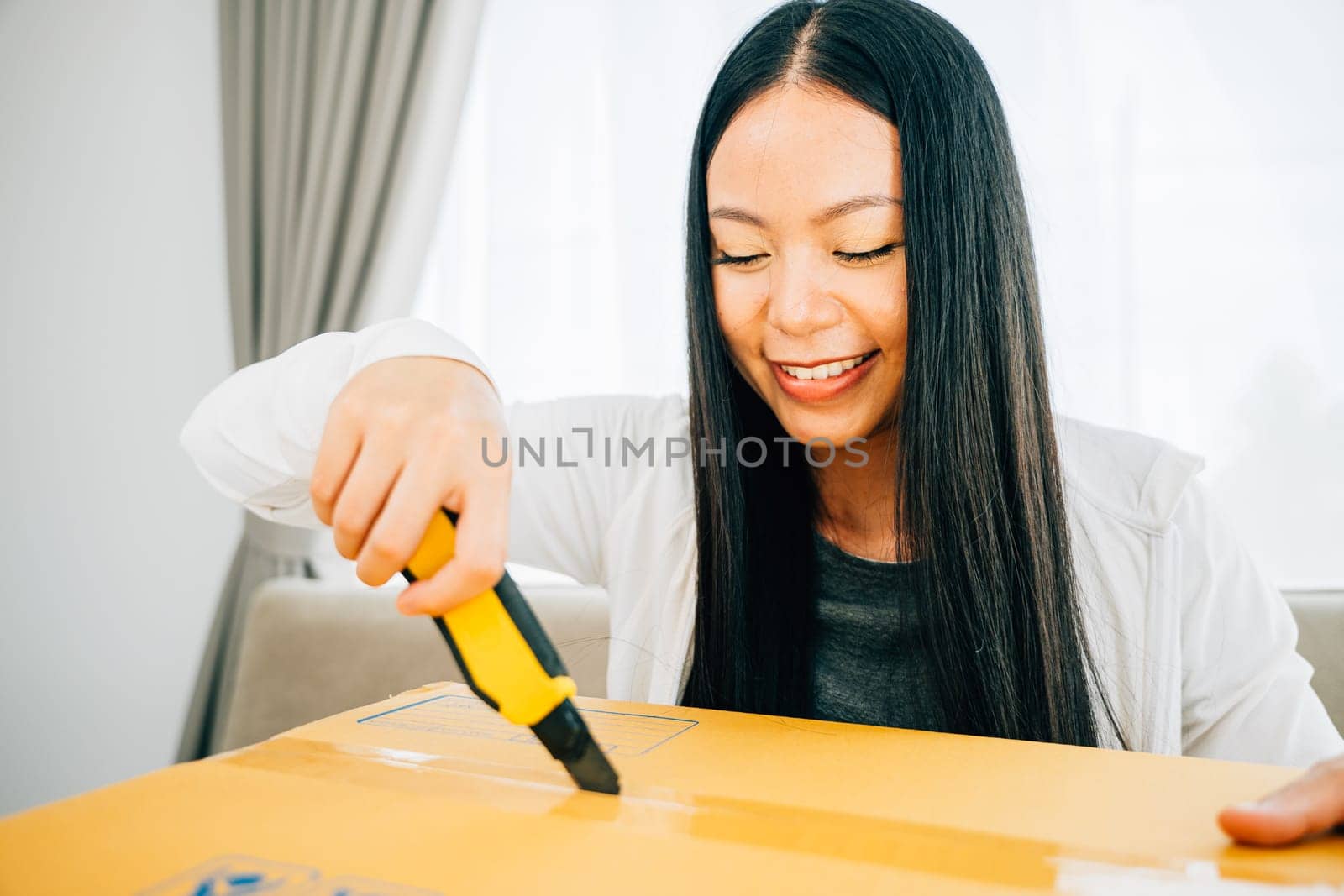 A woman holds a utility cutter for precision unboxing revealing online shopping contents by Sorapop