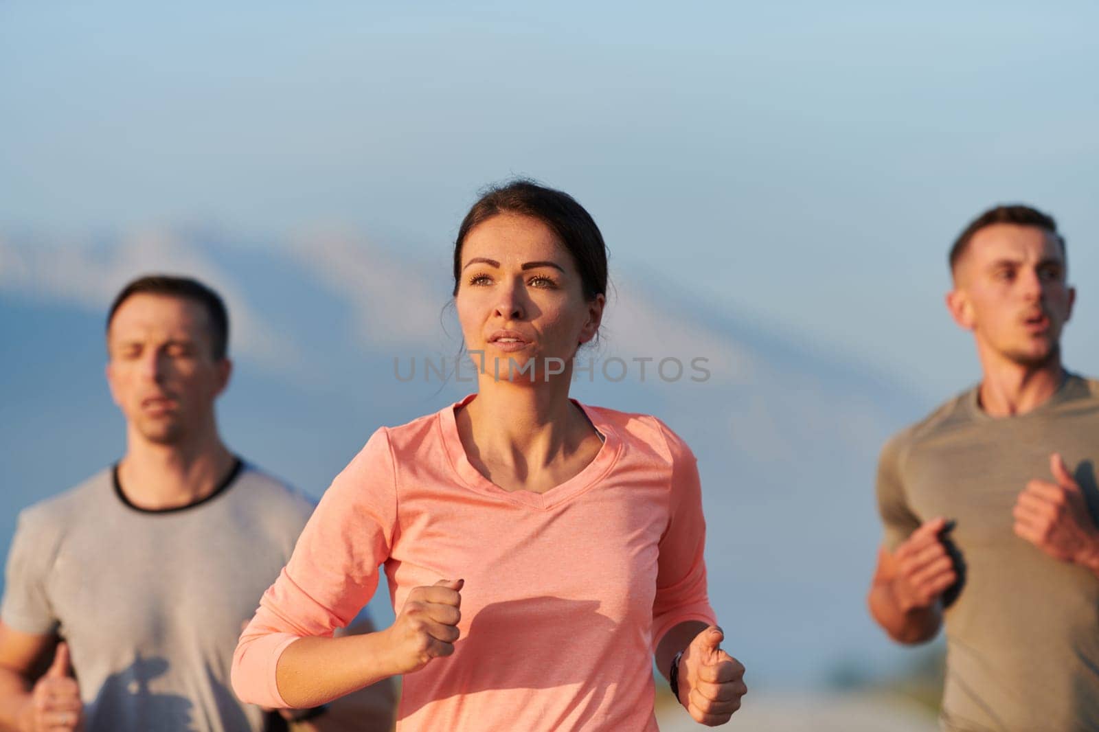 A group of friends, athletes, and joggers embrace the early morning hours as they run through the misty dawn, energized by the rising sun and surrounded by the tranquil beauty of nature.