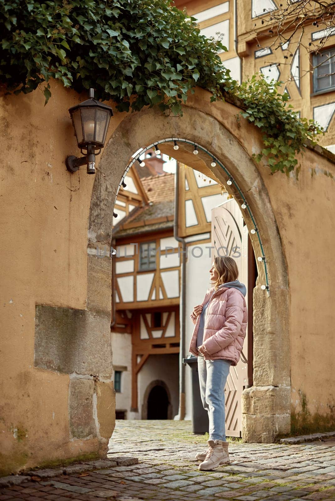 Winter Fun in Bitigheim-Bissingen: Beautiful Girl in Pink Jacket Amidst Half-Timbered Charm. a lovely girl in a pink winter jacket standing in the archway of the historic town of Bitigheim-Bissingen, Baden-Württemberg, Germany. by Andrii_Ko