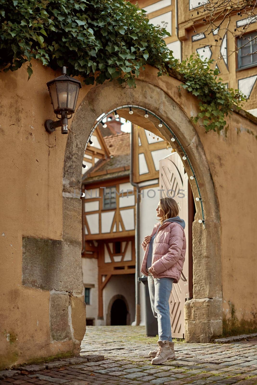 Winter Fun in Bitigheim-Bissingen: Beautiful Girl in Pink Jacket Amidst Half-Timbered Charm. a lovely girl in a pink winter jacket standing in the archway of the historic town of Bitigheim-Bissingen, Baden-Württemberg, Germany. by Andrii_Ko