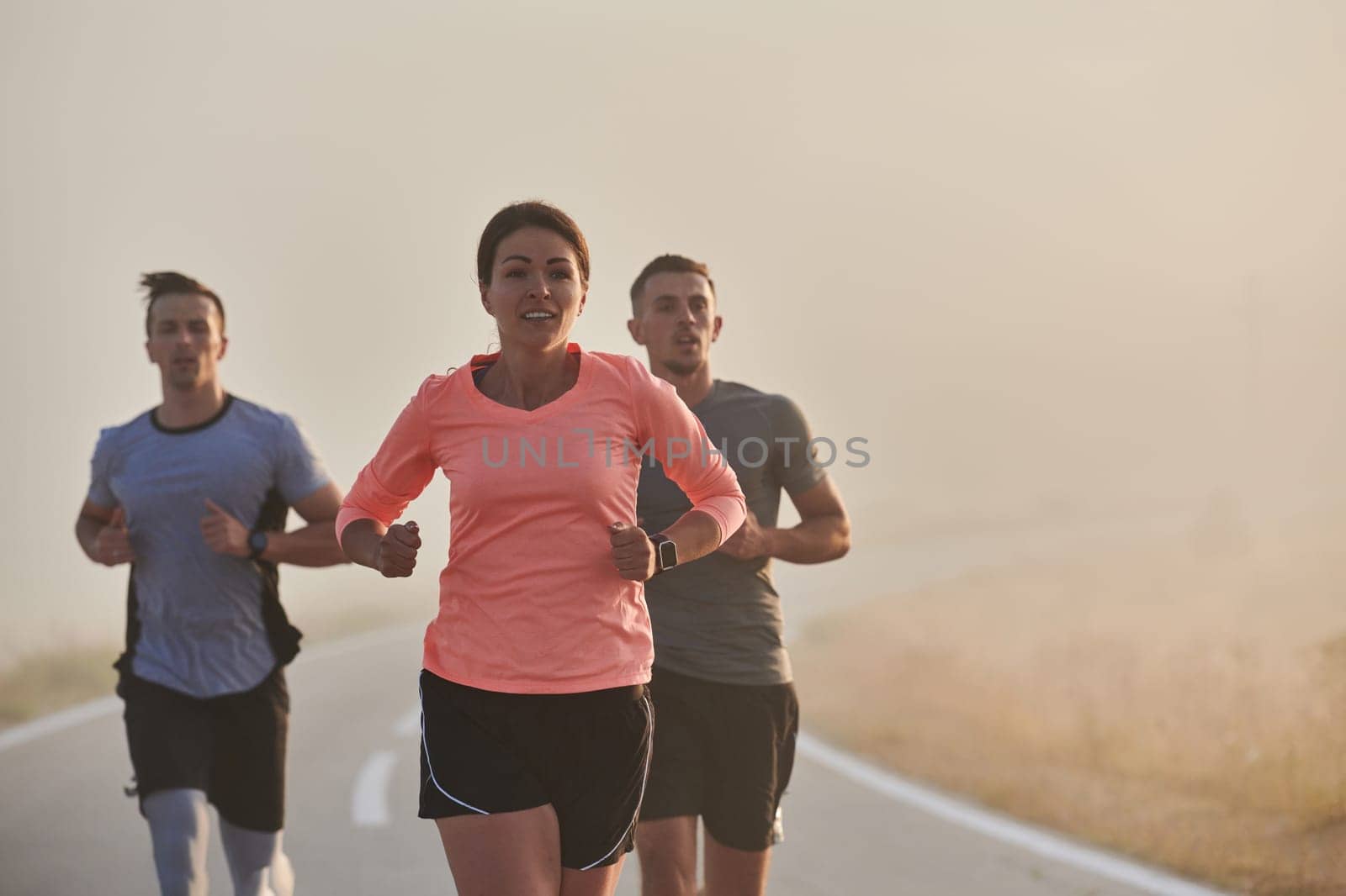 A group of friends, athletes, and joggers embrace the early morning hours as they run through the misty dawn, energized by the rising sun and surrounded by the tranquil beauty of nature.